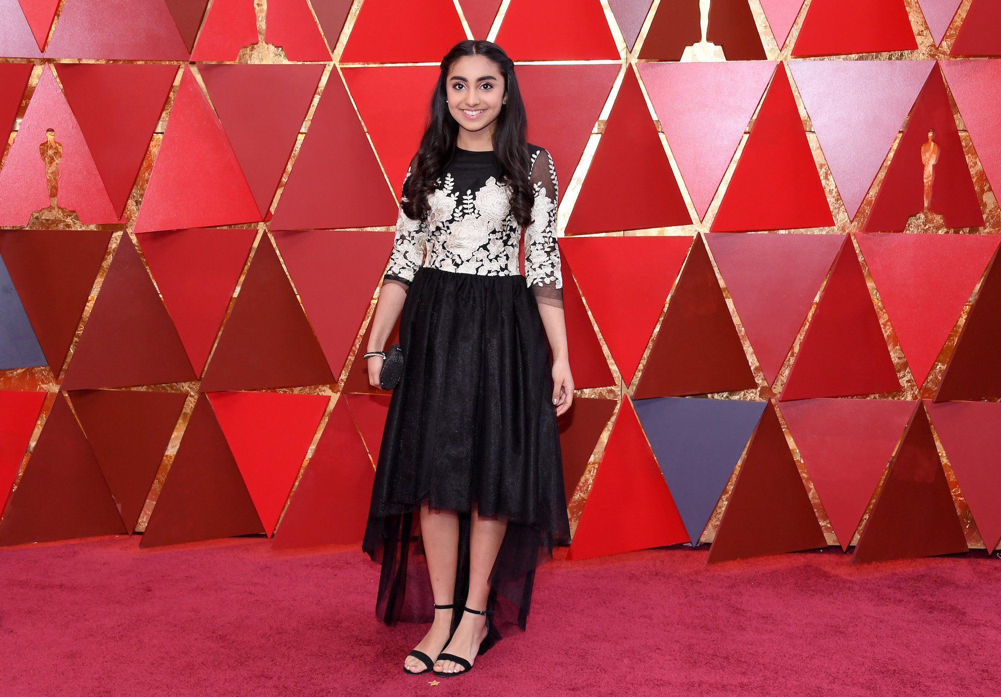 Saara Chaudry smiling on the red carpet in front of a red wall