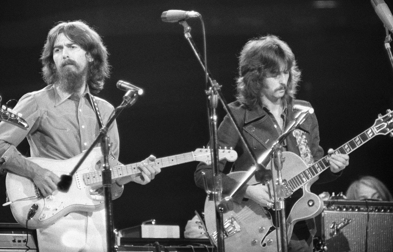 George Harrison and Eric Clapton play guitars onstage.