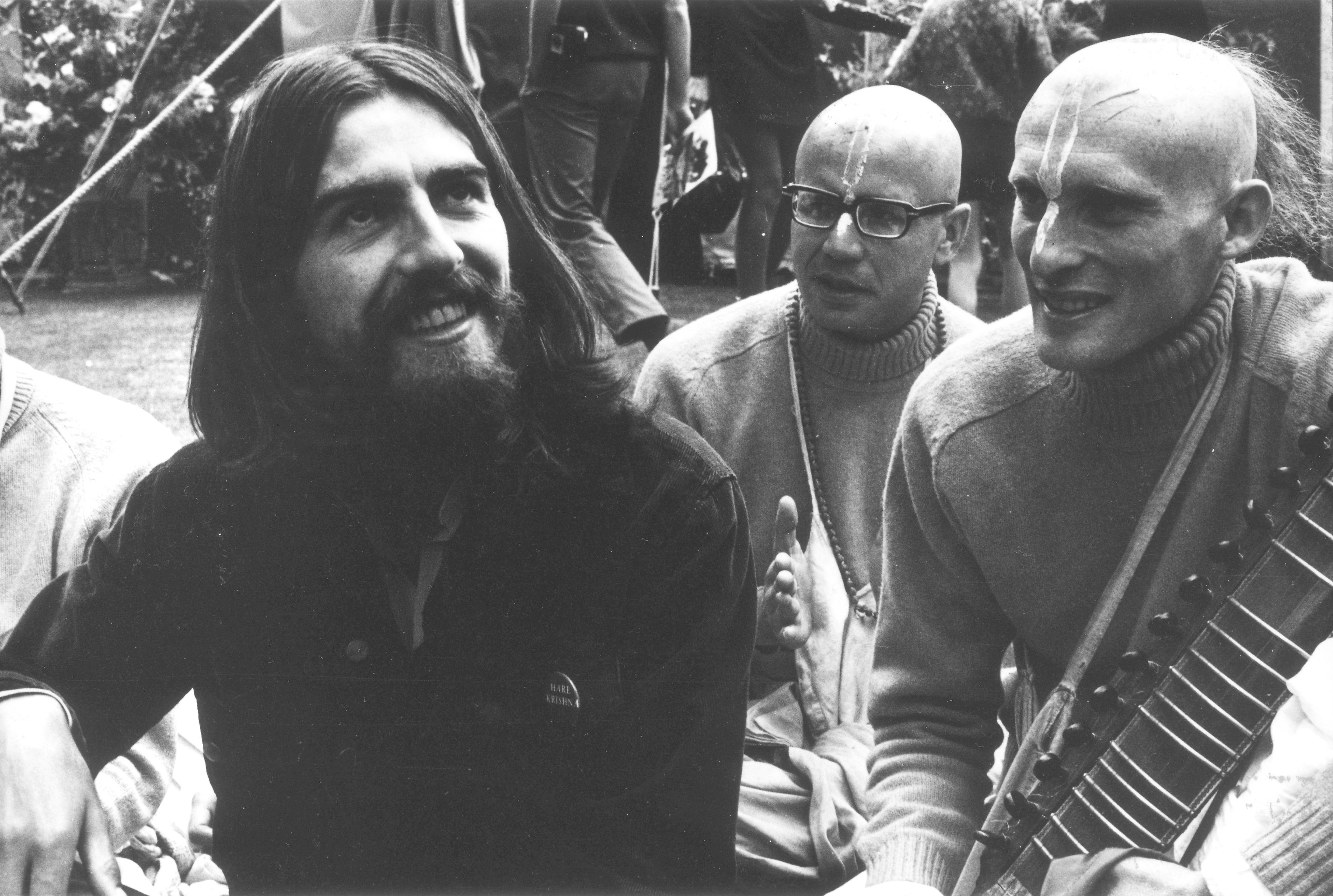 George Harrison sitting next to two men with shaved heads