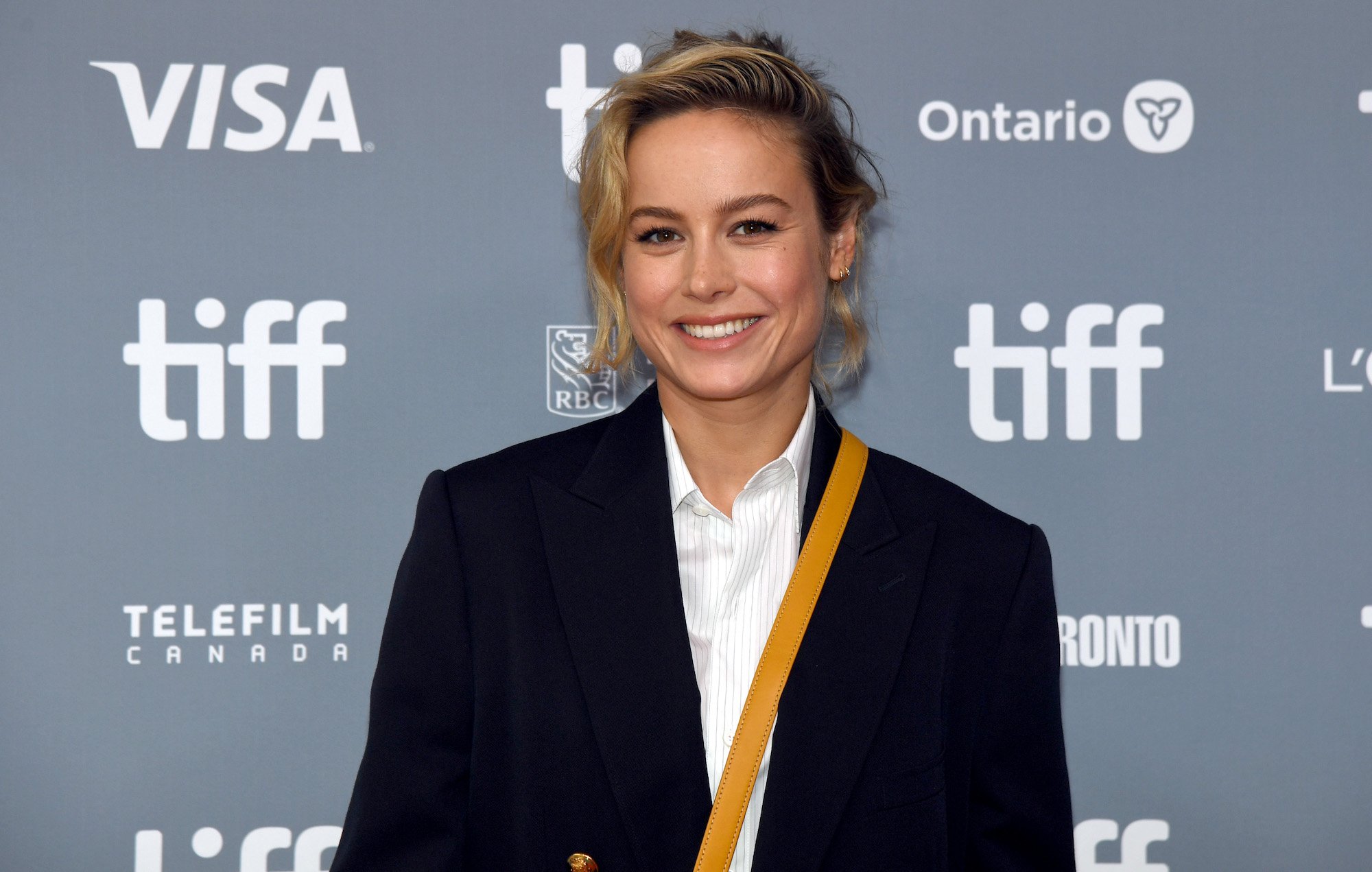 Brie Larson smiling in front of a blue gray background