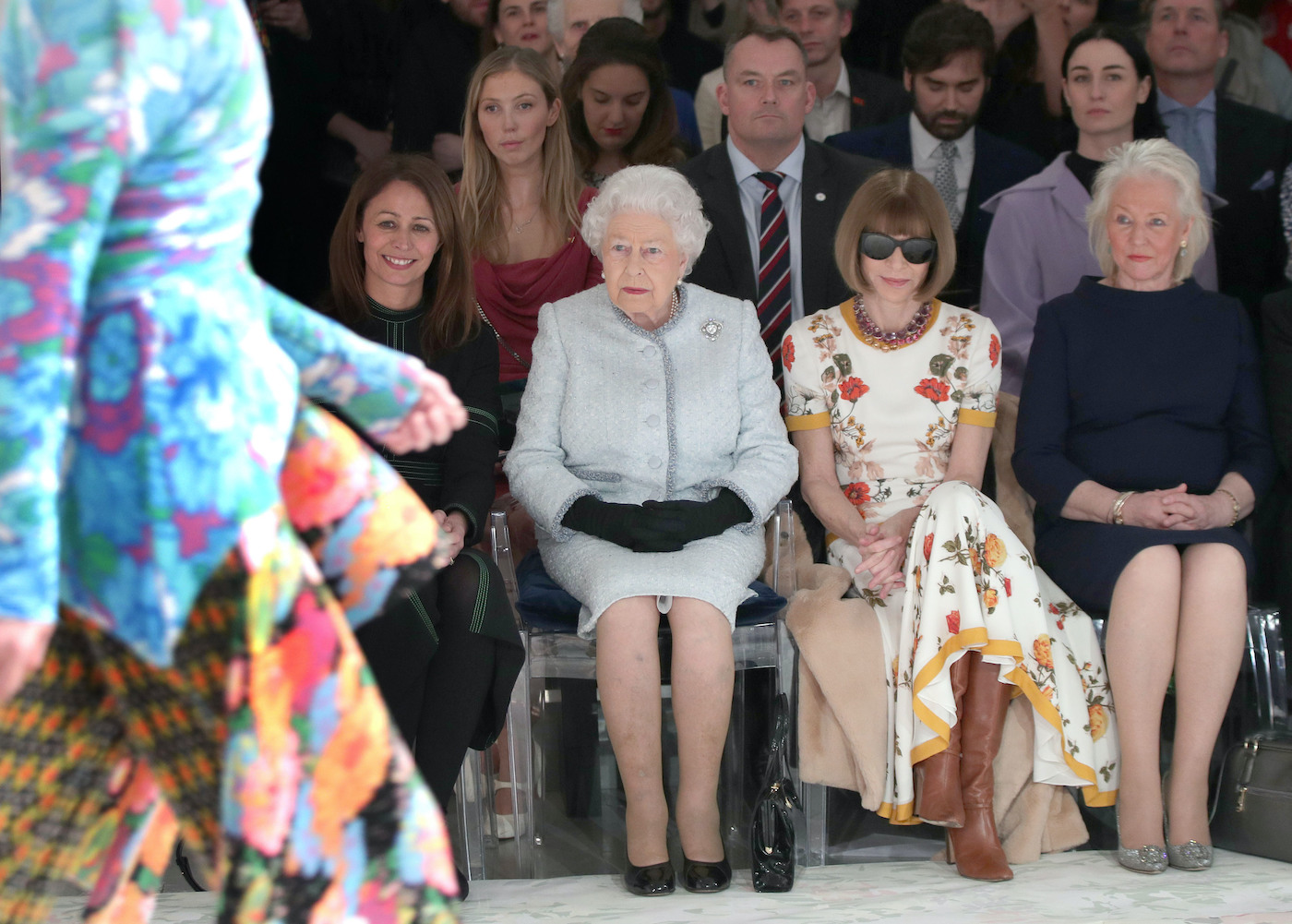 Caroline Rush, Queen Elizabeth II, Anna Wintour, and Angela Kelly sit in the front row of a fashion show