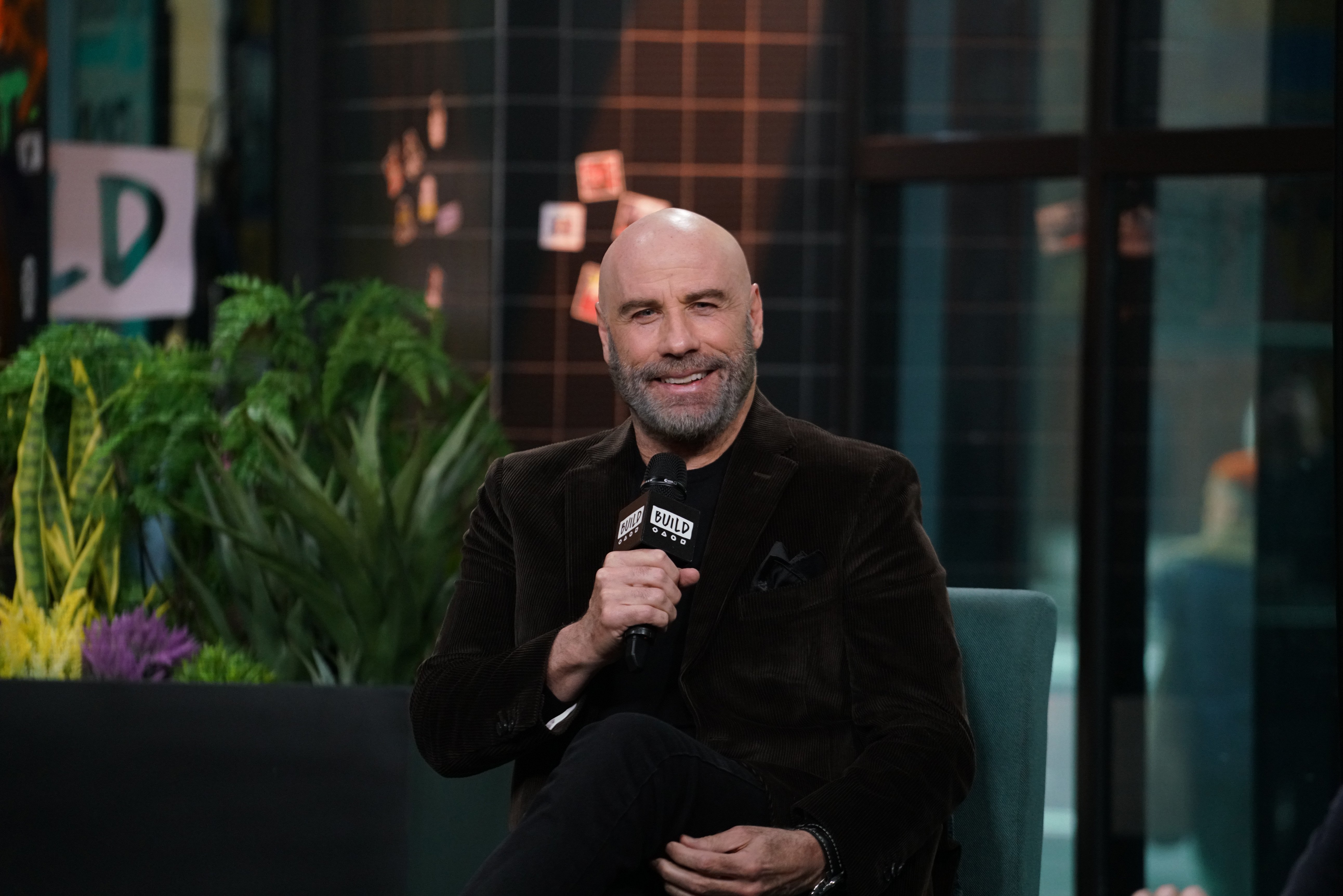 John Travolta smiling holding a microphone