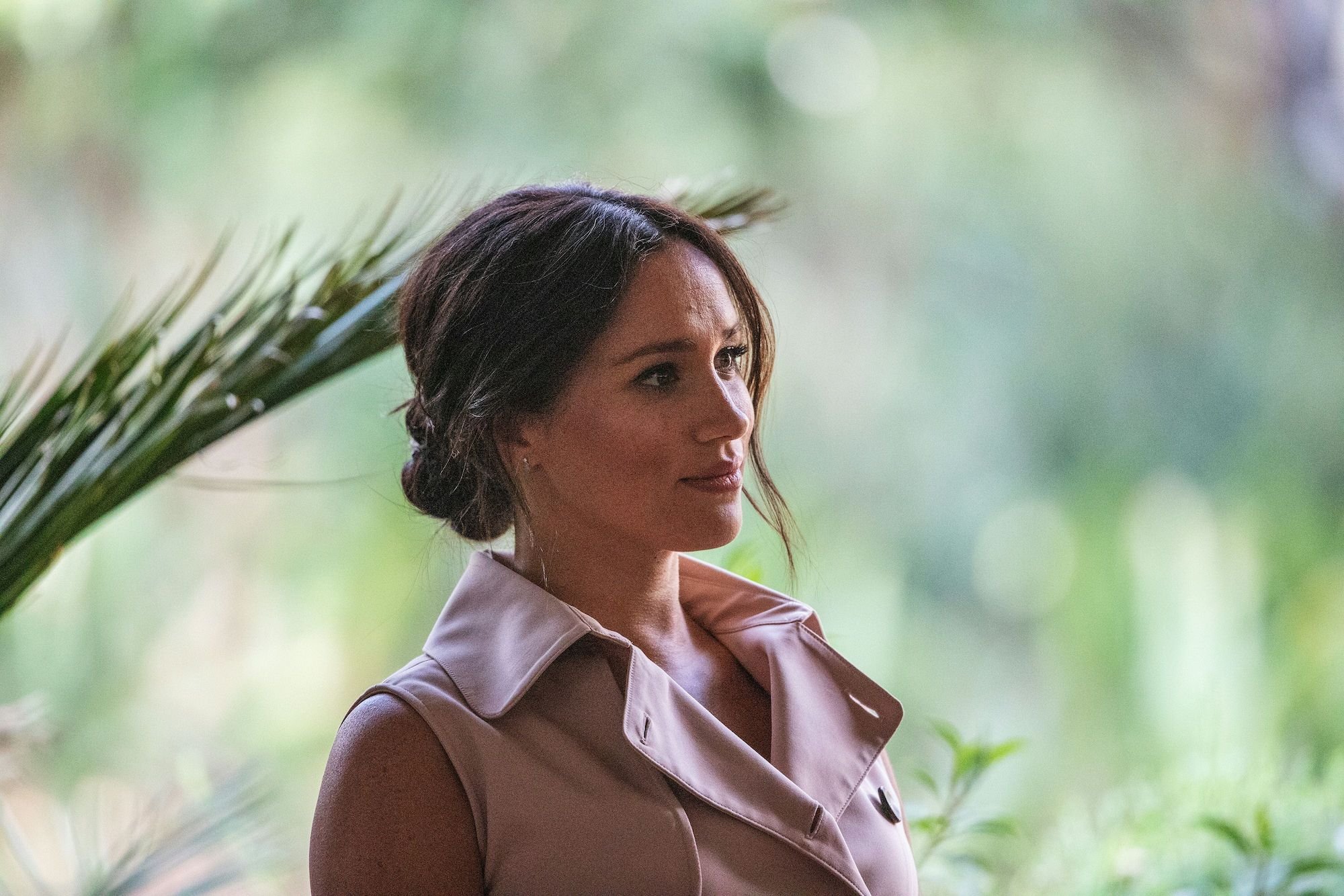 Meghan Markle looking off to the side in front of a blurred green background
