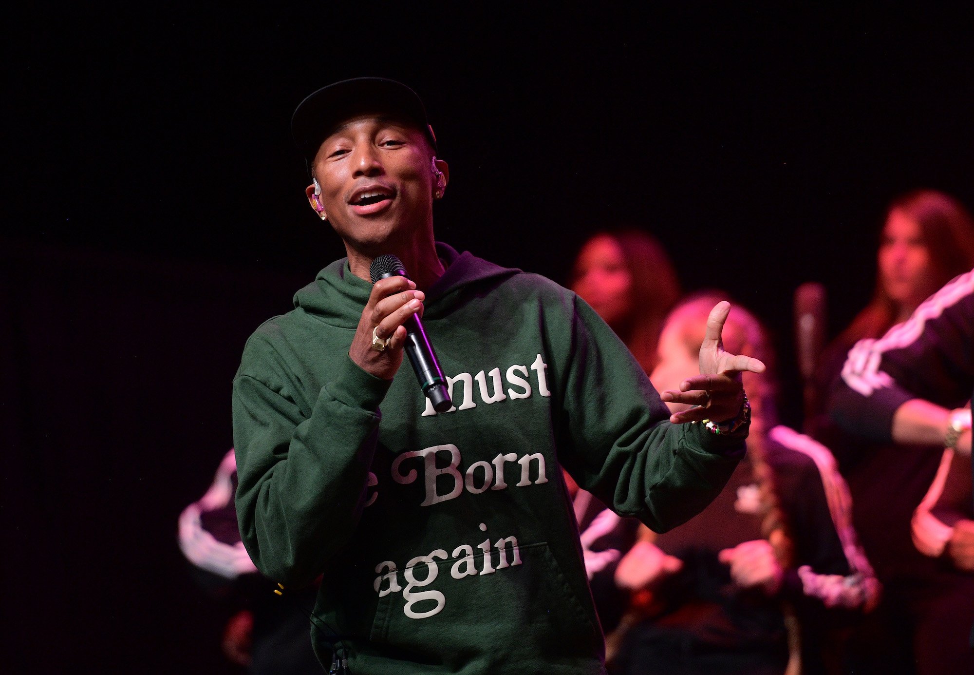 Pharrell Williams smiling on stage, holding a microphone