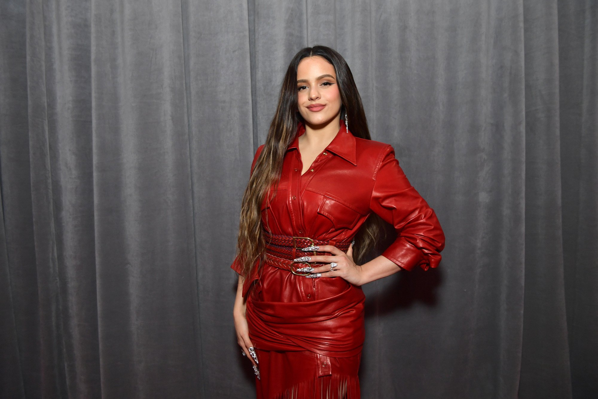 Rosalía smiling at the camera in front of a gray curtain