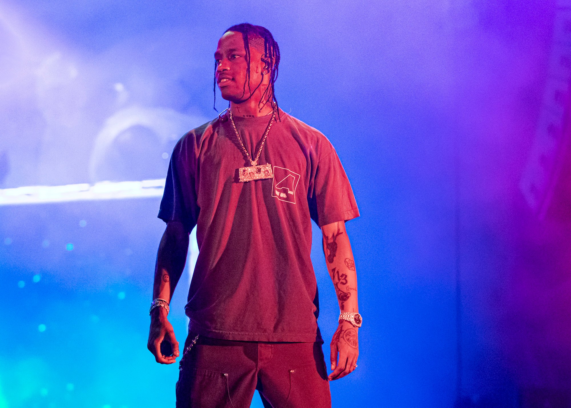 Travis Scott smiling, looking to the side, standing on stage