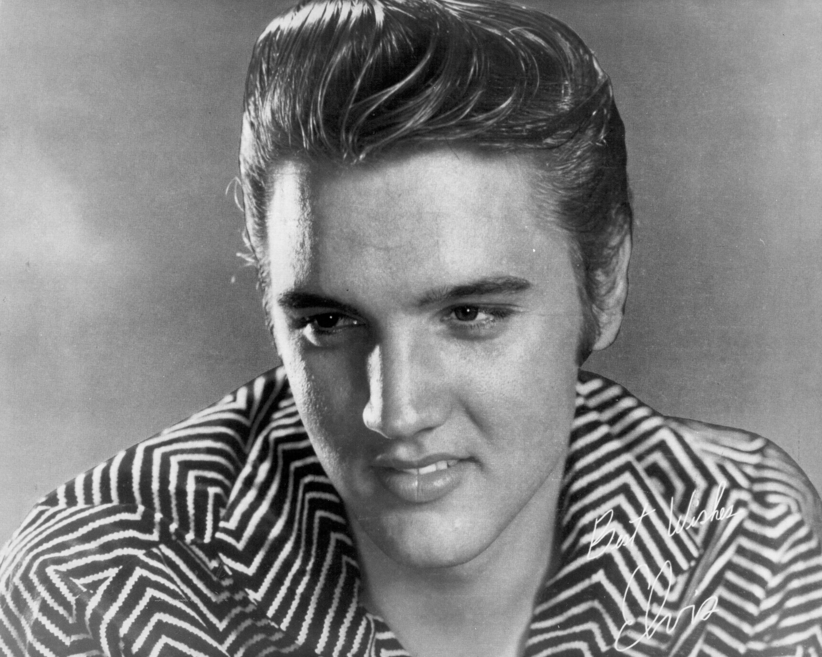 Elvis Presley smiling and wearing a striped shirt in a photo with his signature