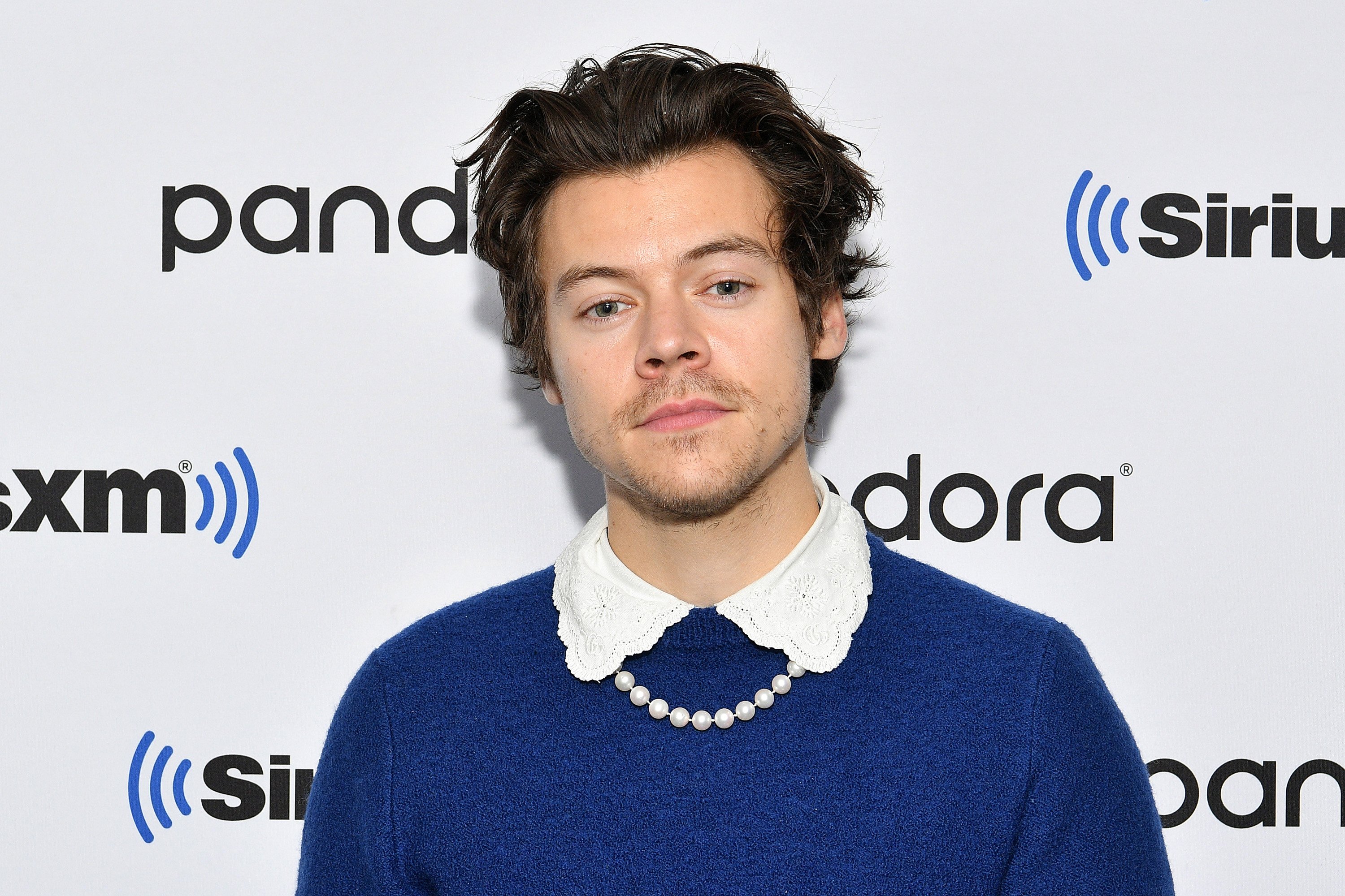 Harry Styles wearing a blue shirt in front of a white background