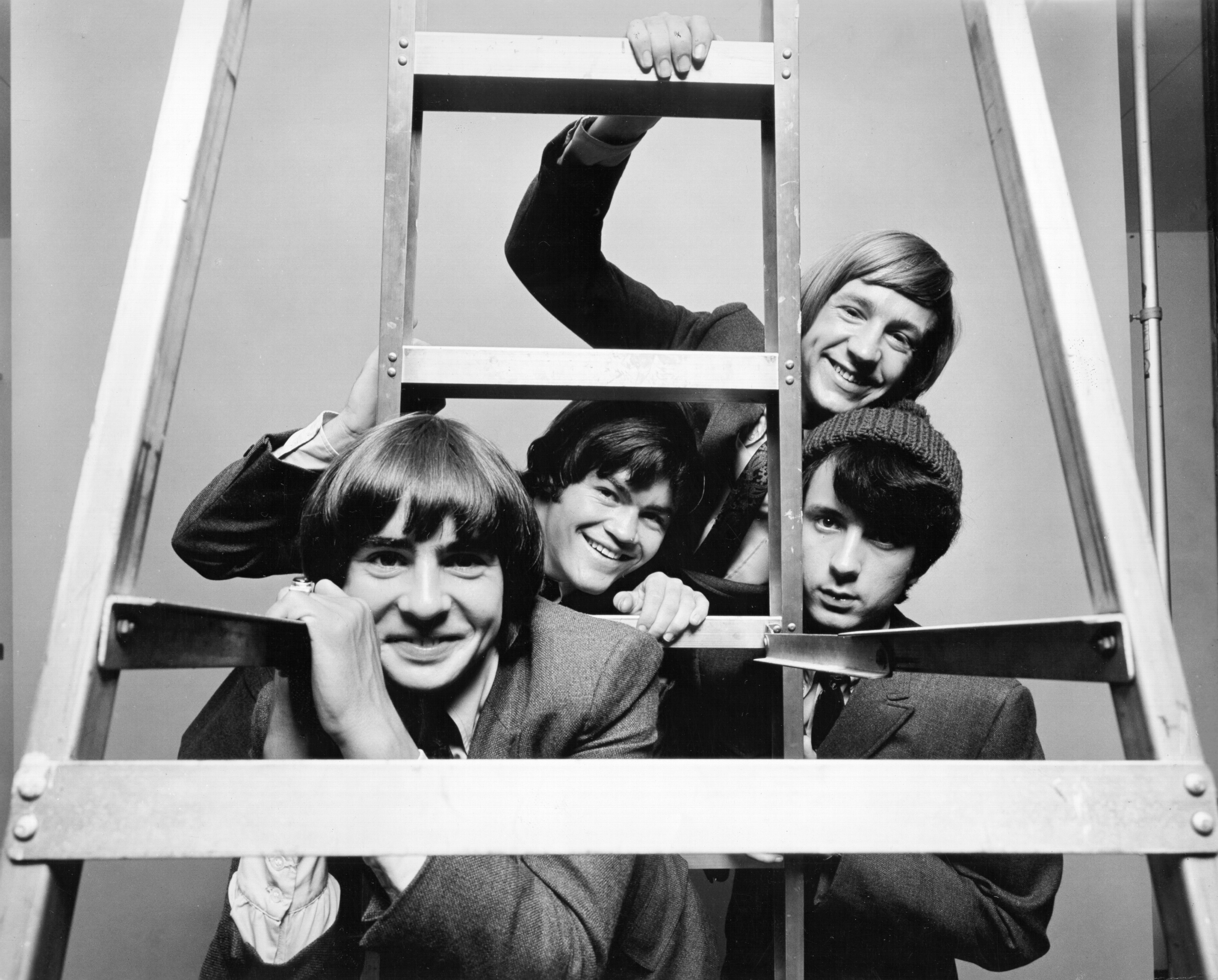 The Monkees peering through the slats of a ladder