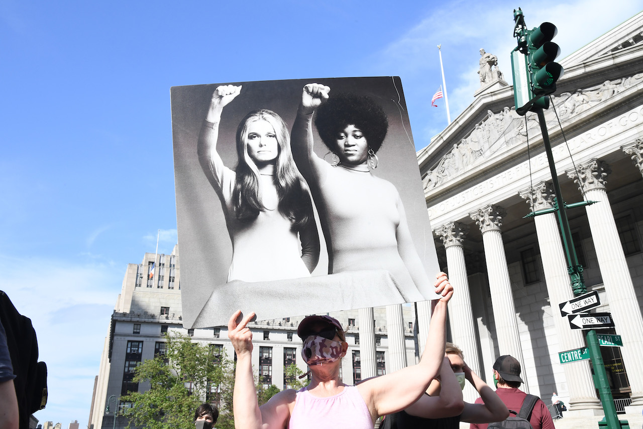 A protester holds a poster that shows an image of Gloria Steinem and Dorothy Pitman Hughes