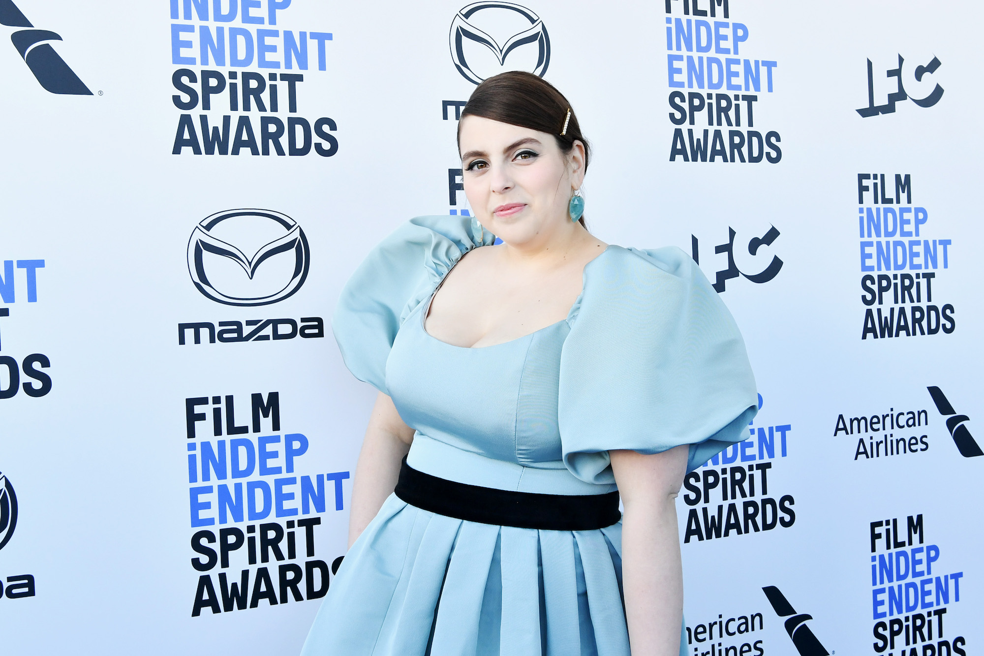 Beanie Feldstein smiling in front of a white and blue background
