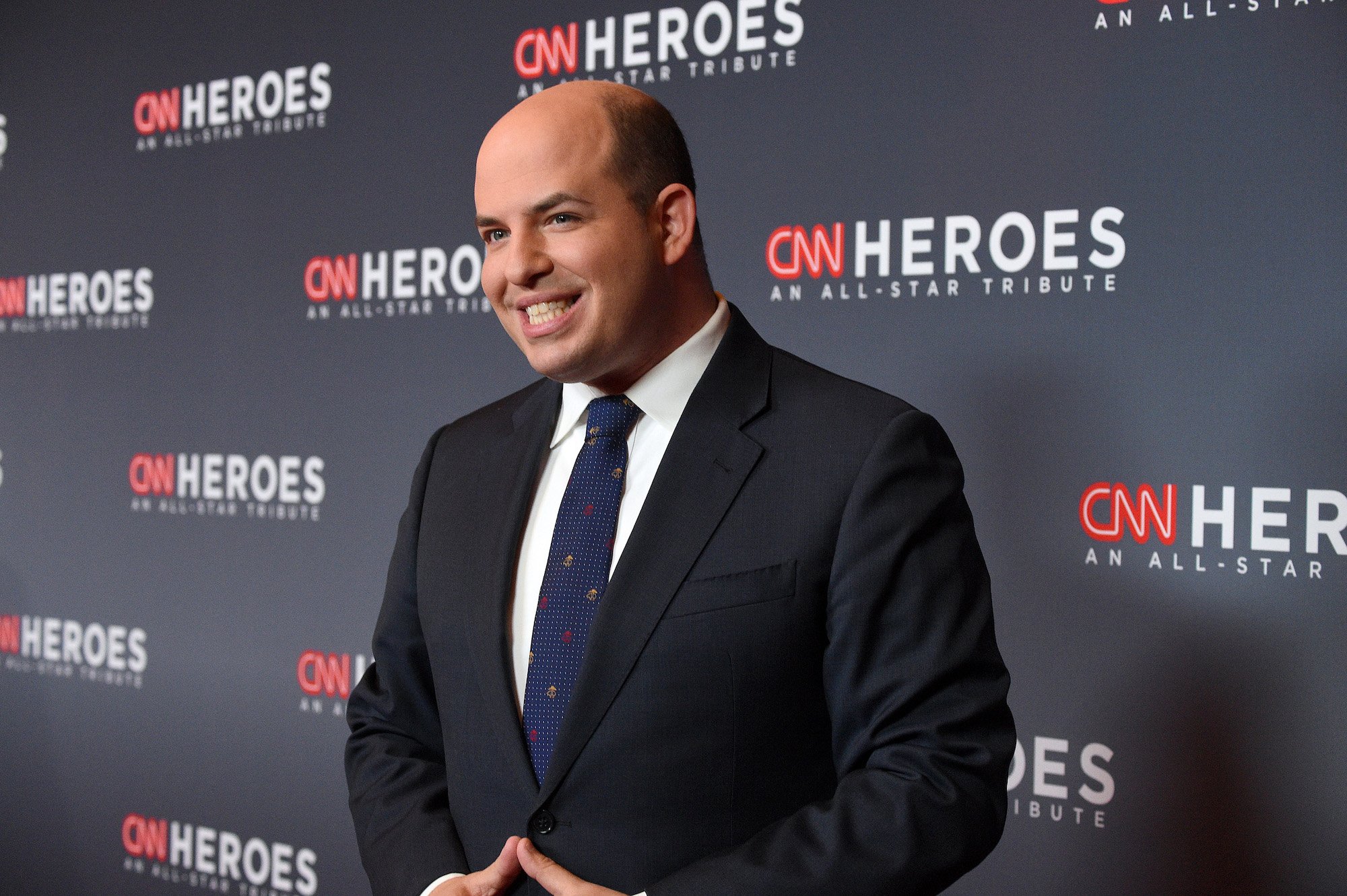 Brian Stelter smiling in front of a dark blue background