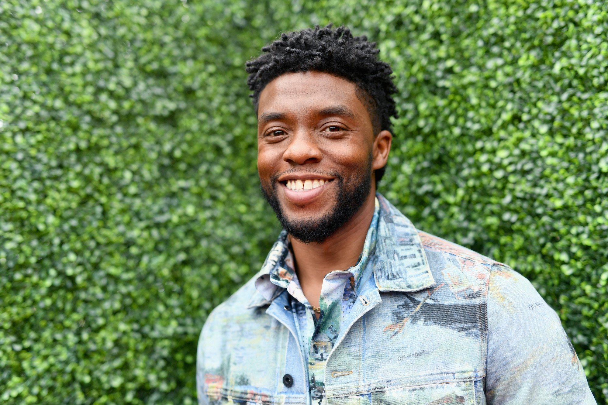 Chadwick Boseman smiling in front of a green background