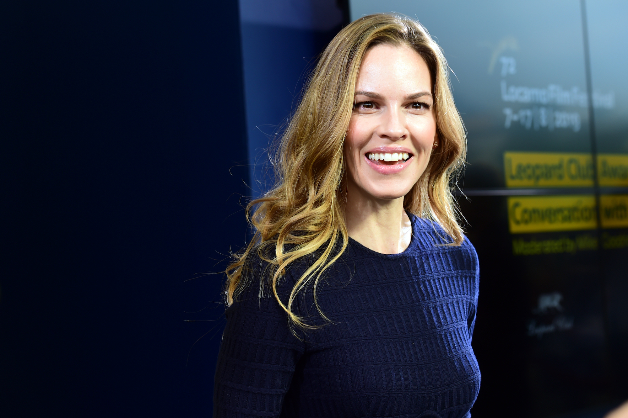 Hilary Swank smiling in front of a blue background