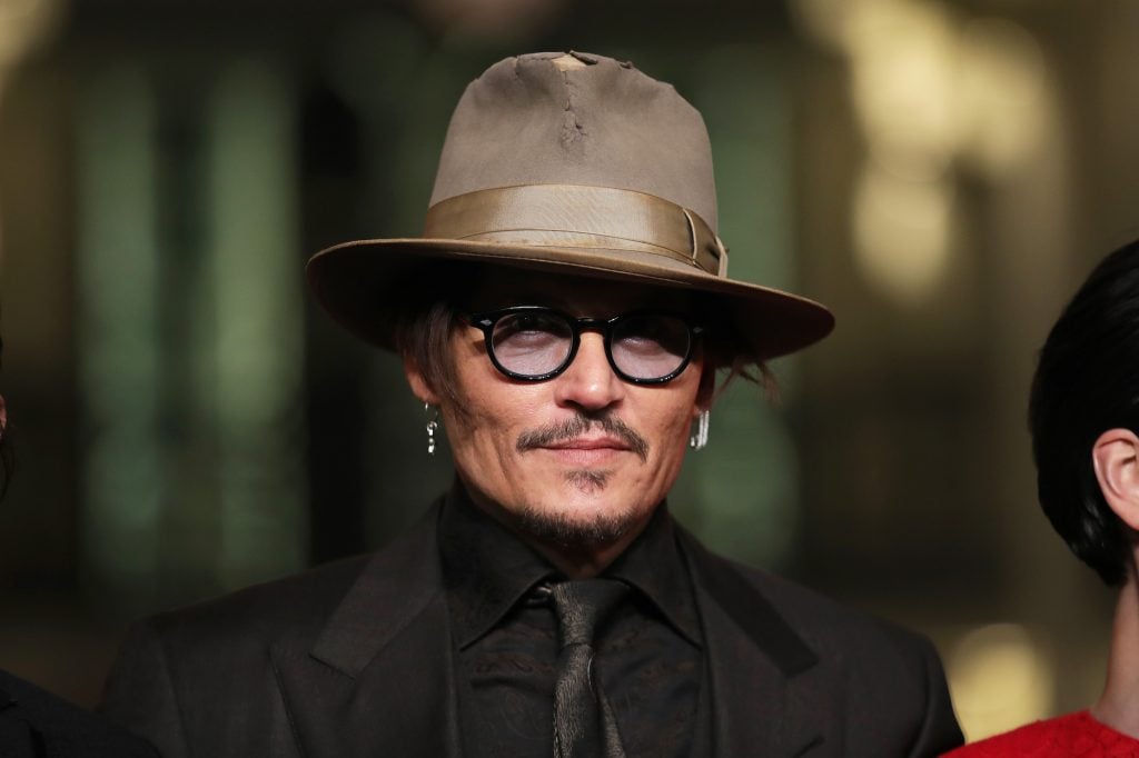 Johnny Depp in a hat and glasses in front of a blurred background