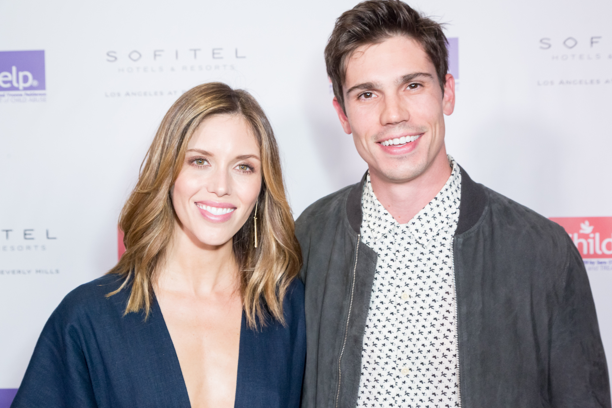 (L-R) Kayla Ewell and Tanner Novlan smiling in front of a white wall