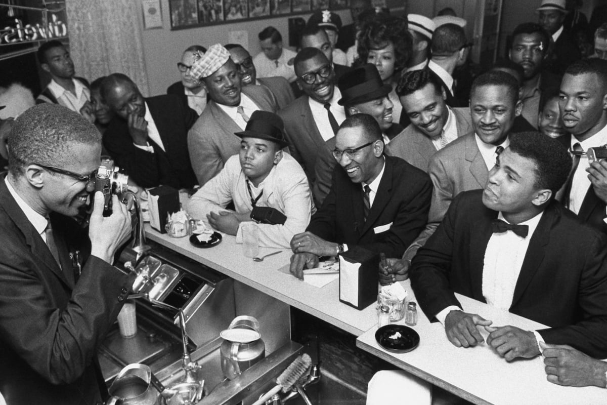MARCH 1964 - MIAMI: Black Muslim leader Malcolm X (L) behind soda fountain training his camera on tux-clad Cassius Clay (now Muhammad Ali) (R) sitting at counter surrounded by jubilant fans after he beat Sonny Liston for the heavyweight championship of the world.