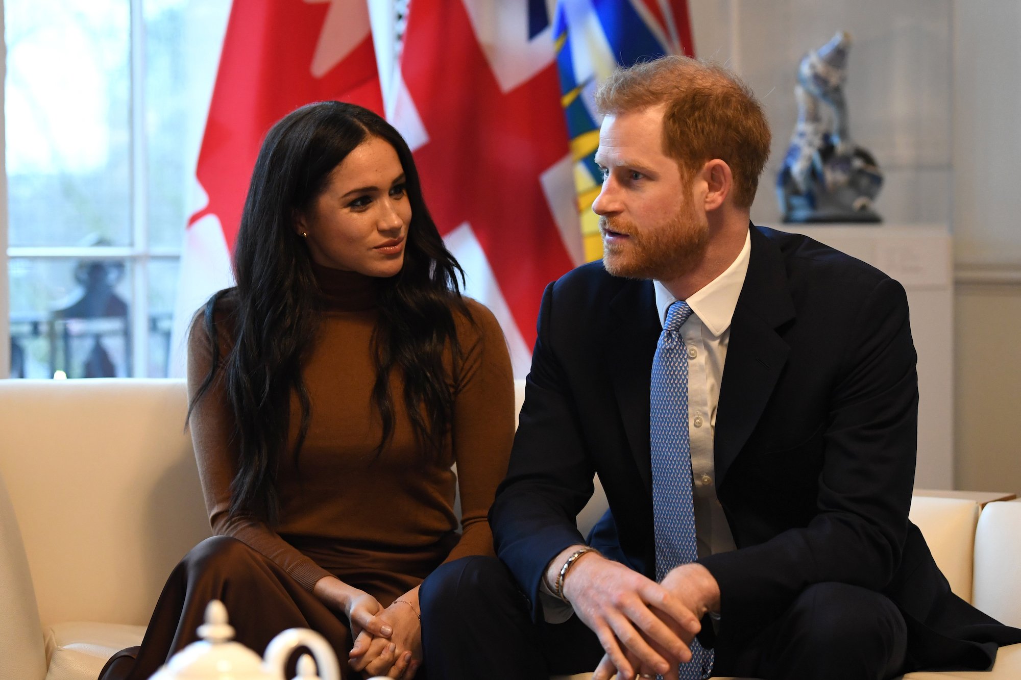 (L-R) Meghan Markle and Prince Harry smiling, seated next to each other in front of a blurred background