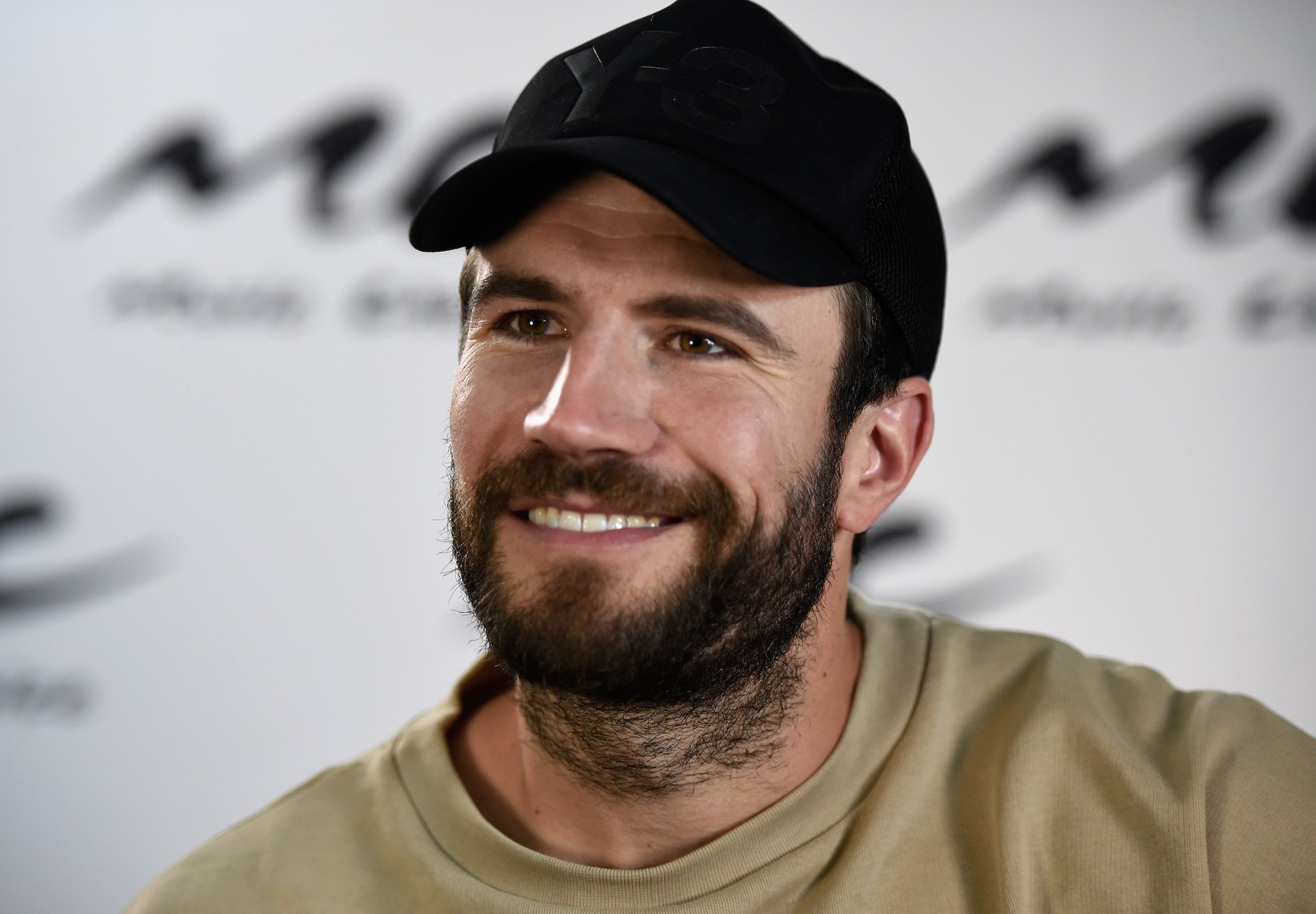 Sam Hunt smiling wearing a black baseball hat