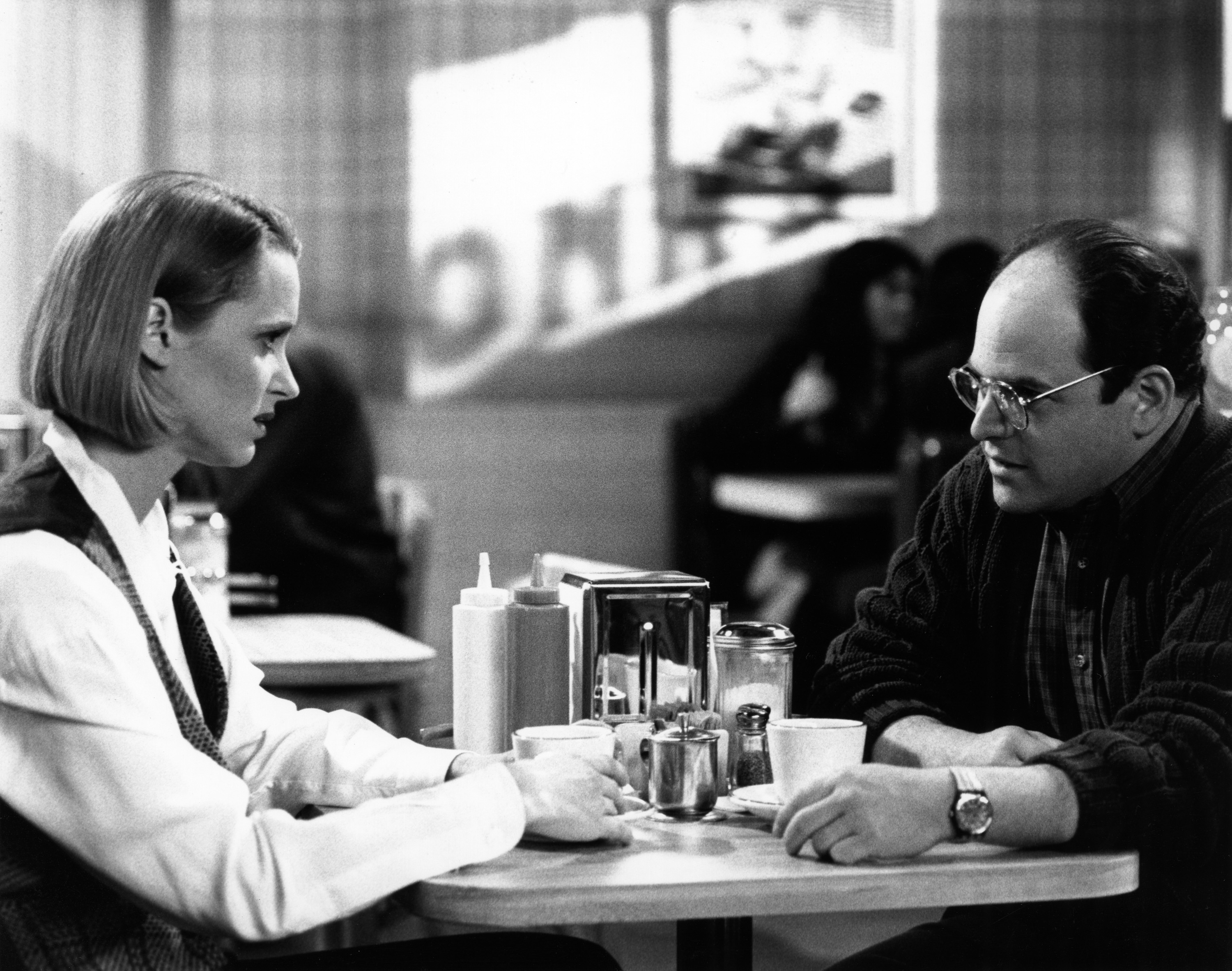 Heidi Swedberg as Susan and Jason Alexander as George sitting across from each other at a diner in a scene from 'Seinfeld.'