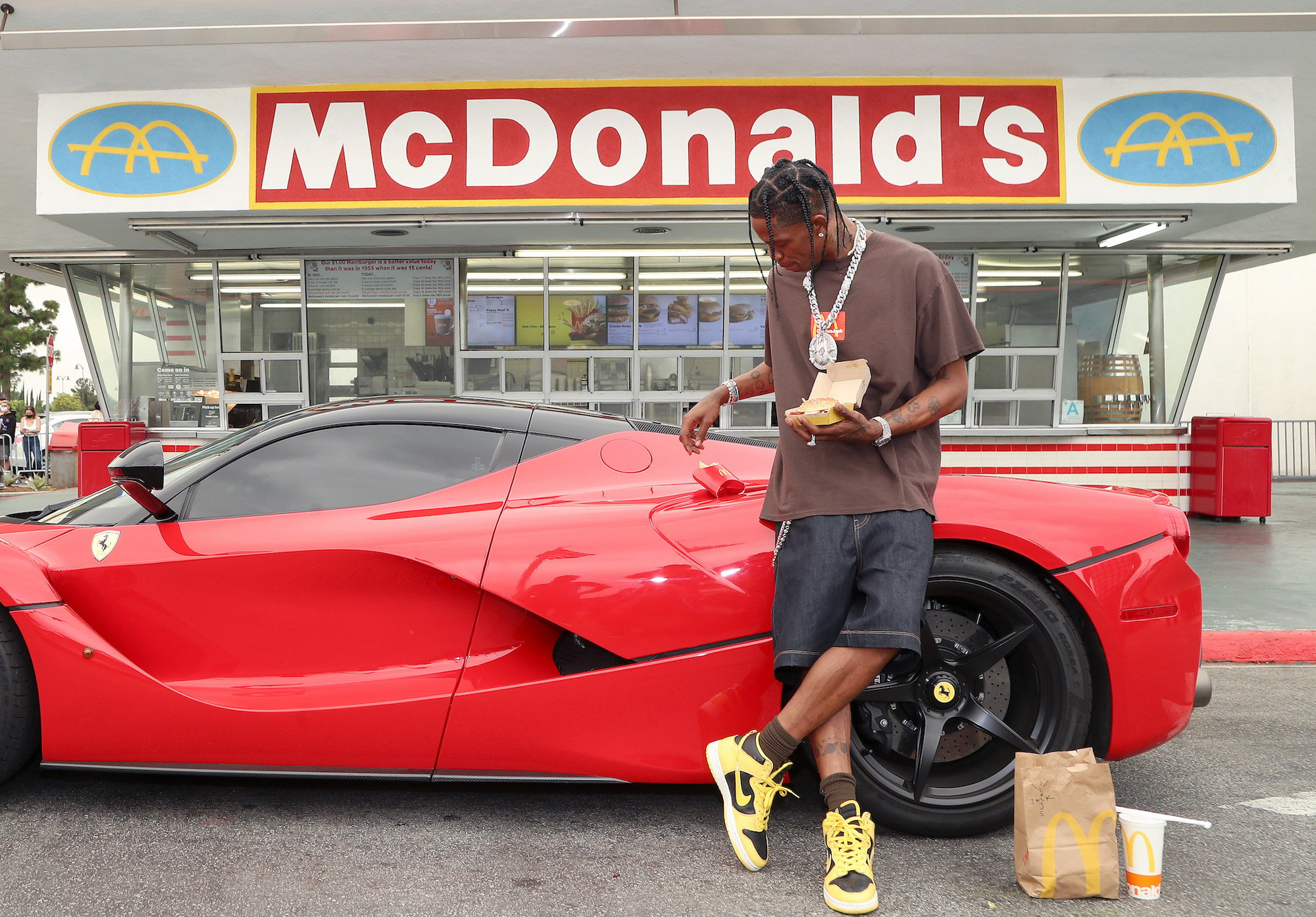 Travis Scott leaning against a red car in front of a McDonald's