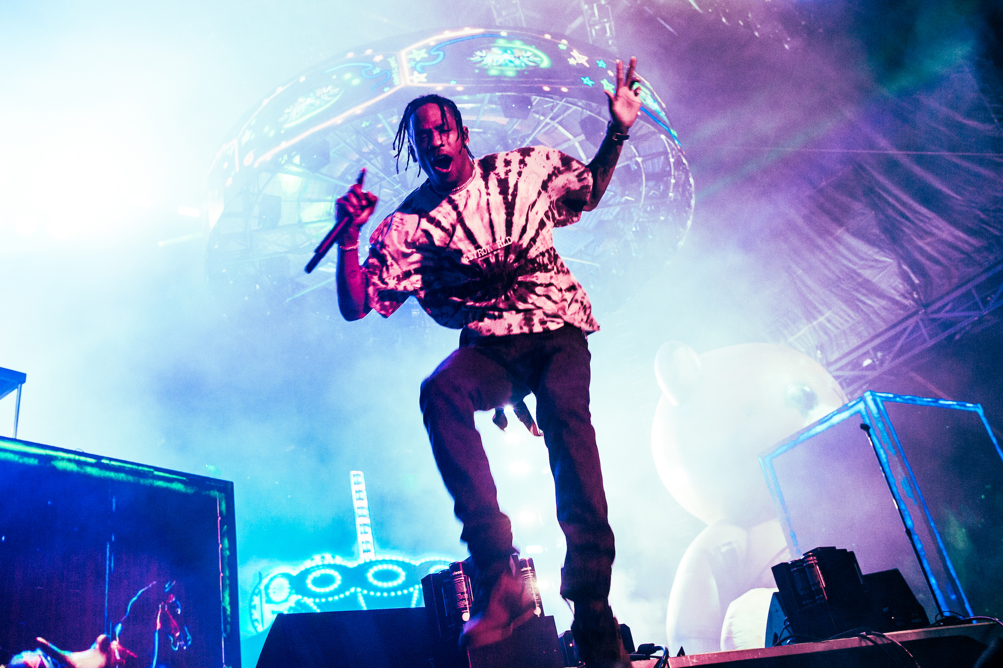 Travis Scott performing on stage with a blue and purple projection behind him