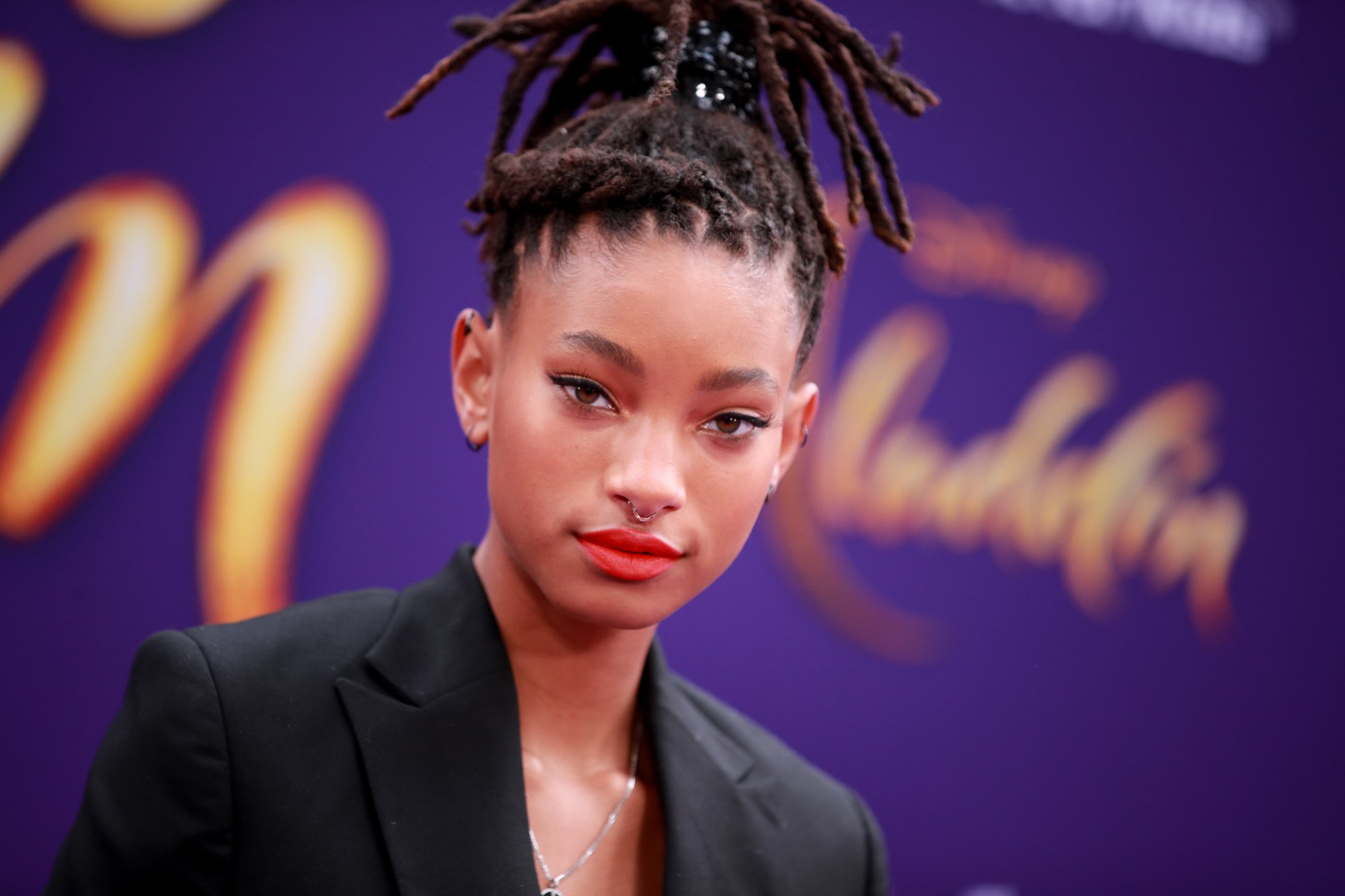 Willow Smith slightly smiling in front of a blurred purple background