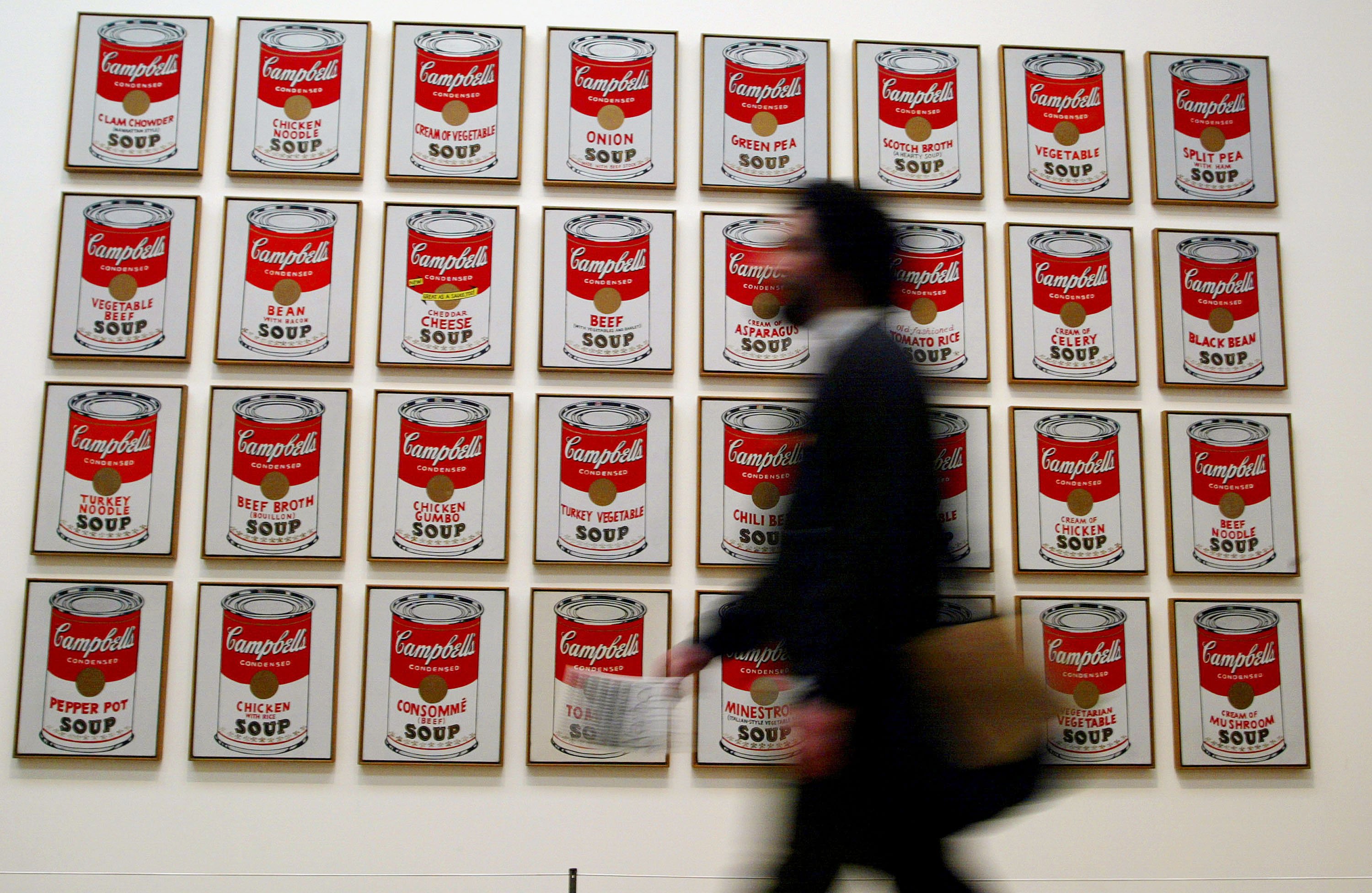 A man walking past Andy Warhol paintings of soup cans