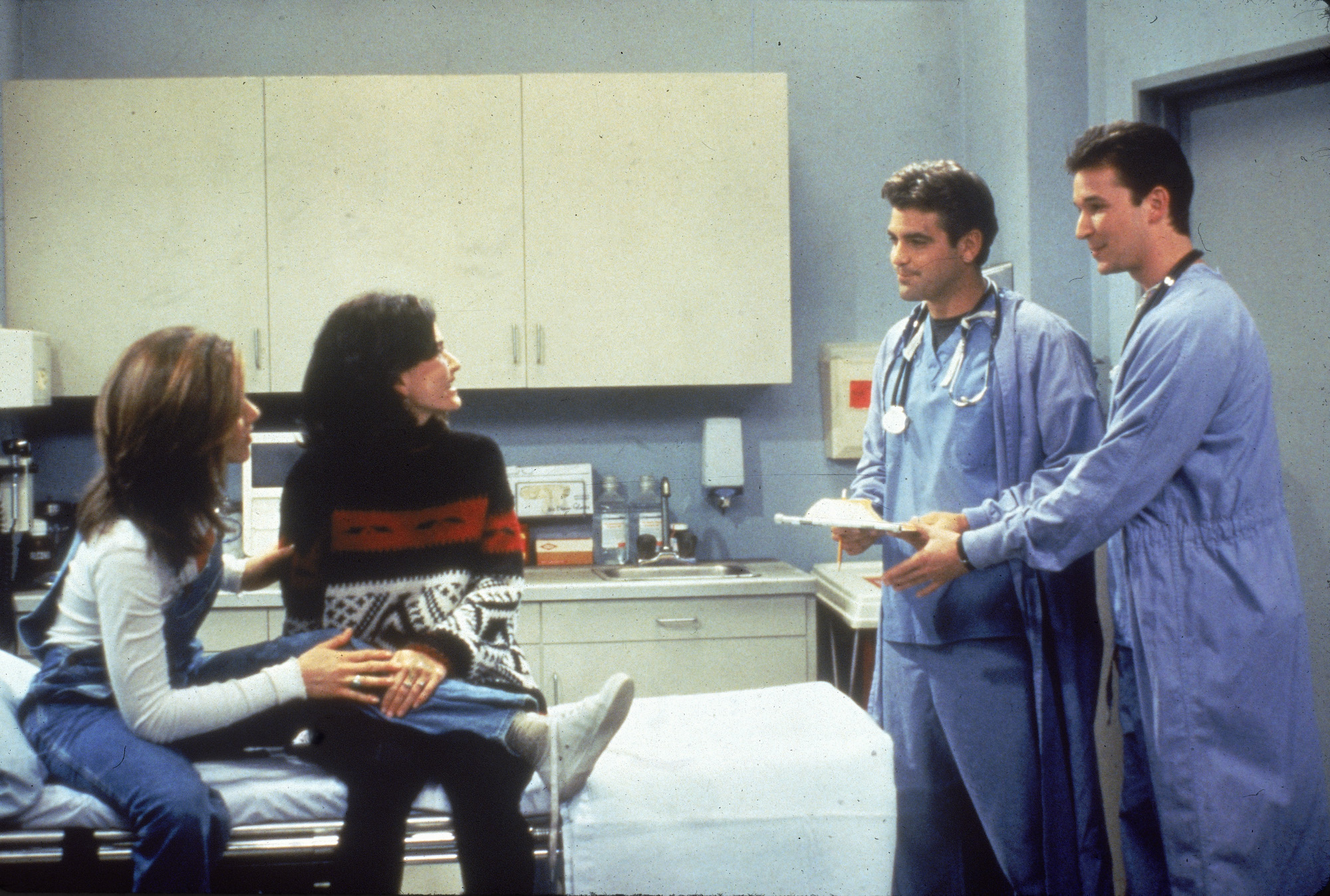 Jennifer Aniston and Courteney Cox sit in a hospital room, speaking to guest stars George Clooney and Noah Wyle from 'ER' 