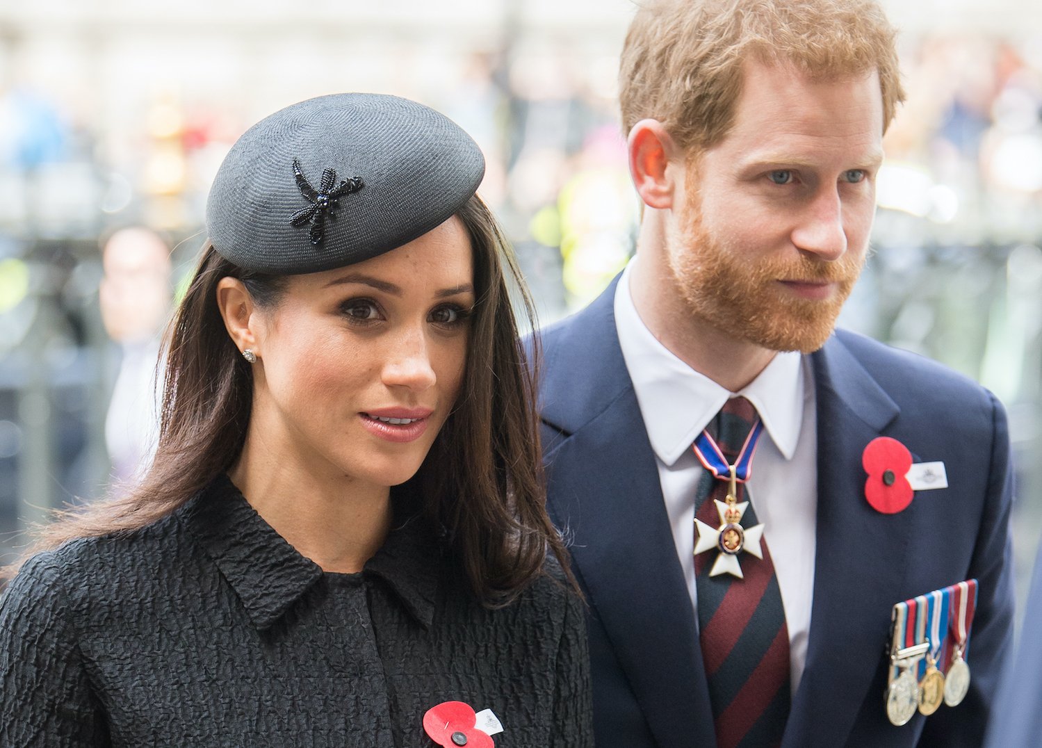 Meghan Markle wearing a black beret next to Prince Harry in a suit with medal decorations