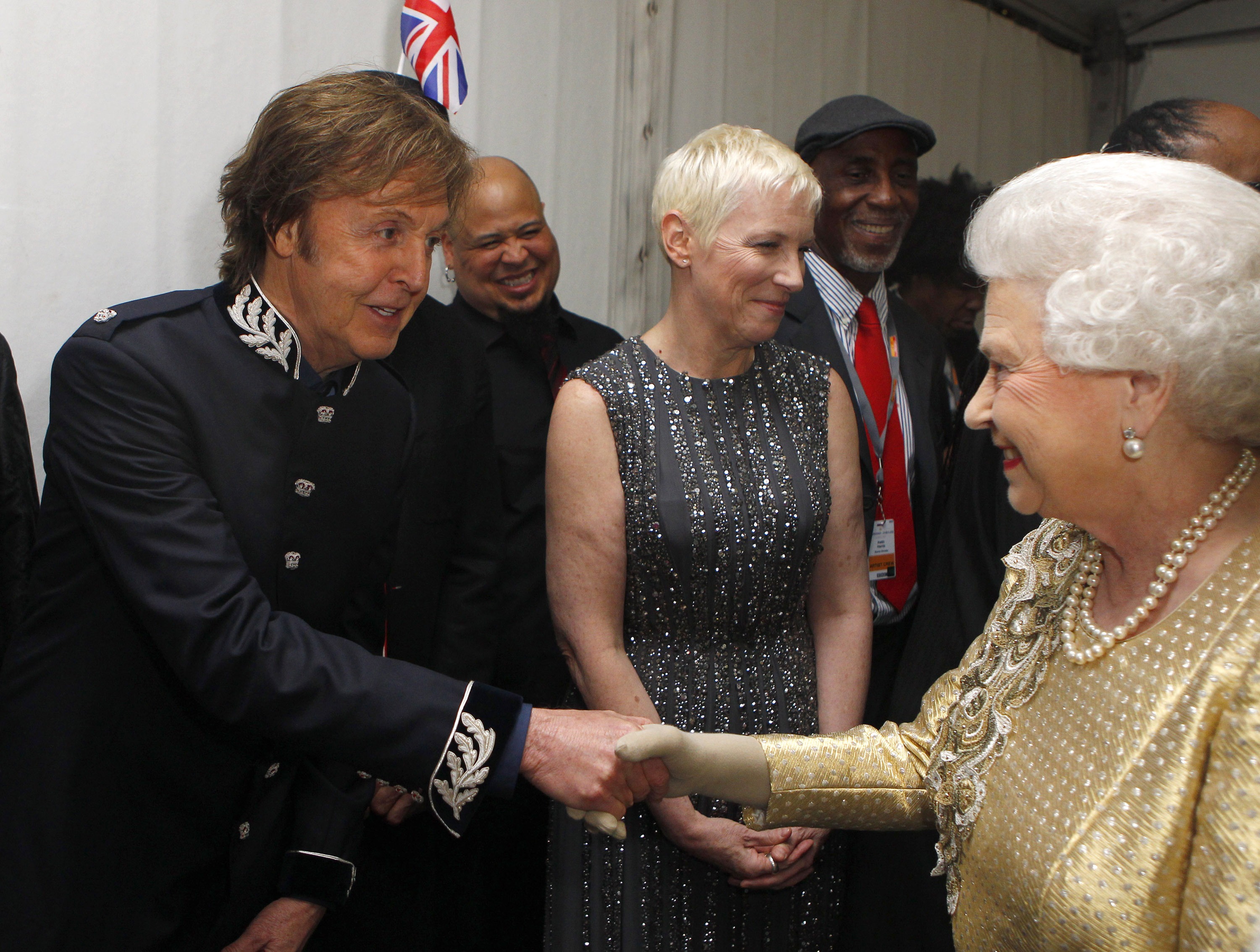 Queen Elizabeth II shaking hands with Paul McCartney in front of Annie Lennox