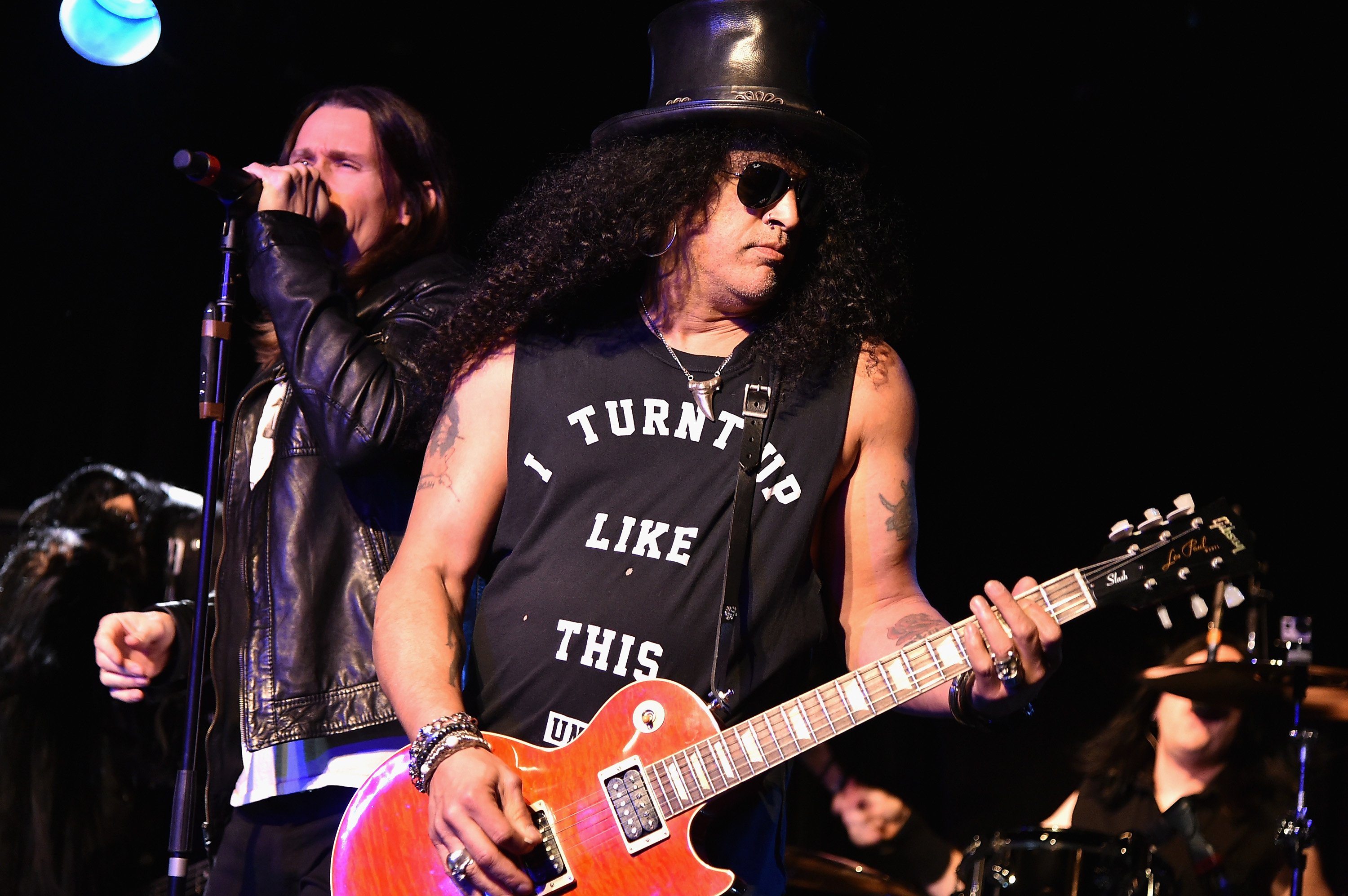 Myles Kennedy singing into a microphone next to Slash with a guitar