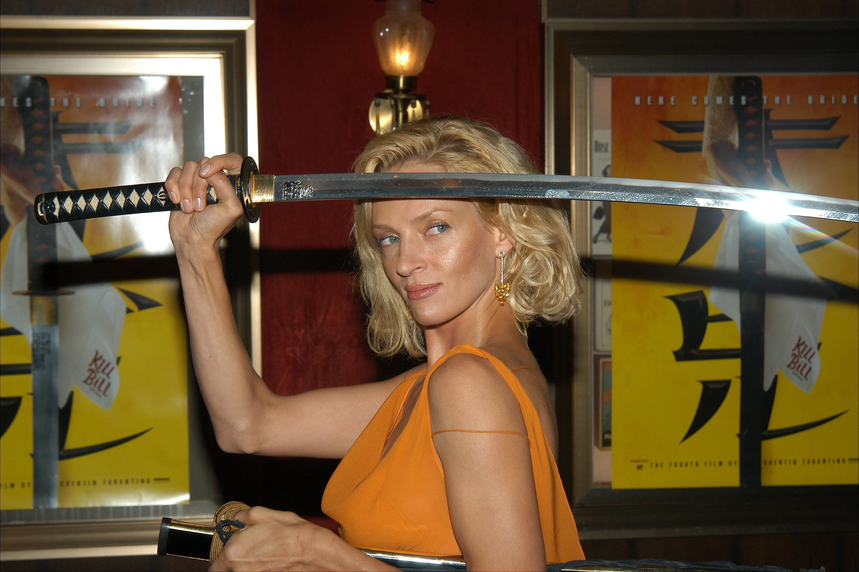 Uma Thurman holding a sword near Kill Bill posters
