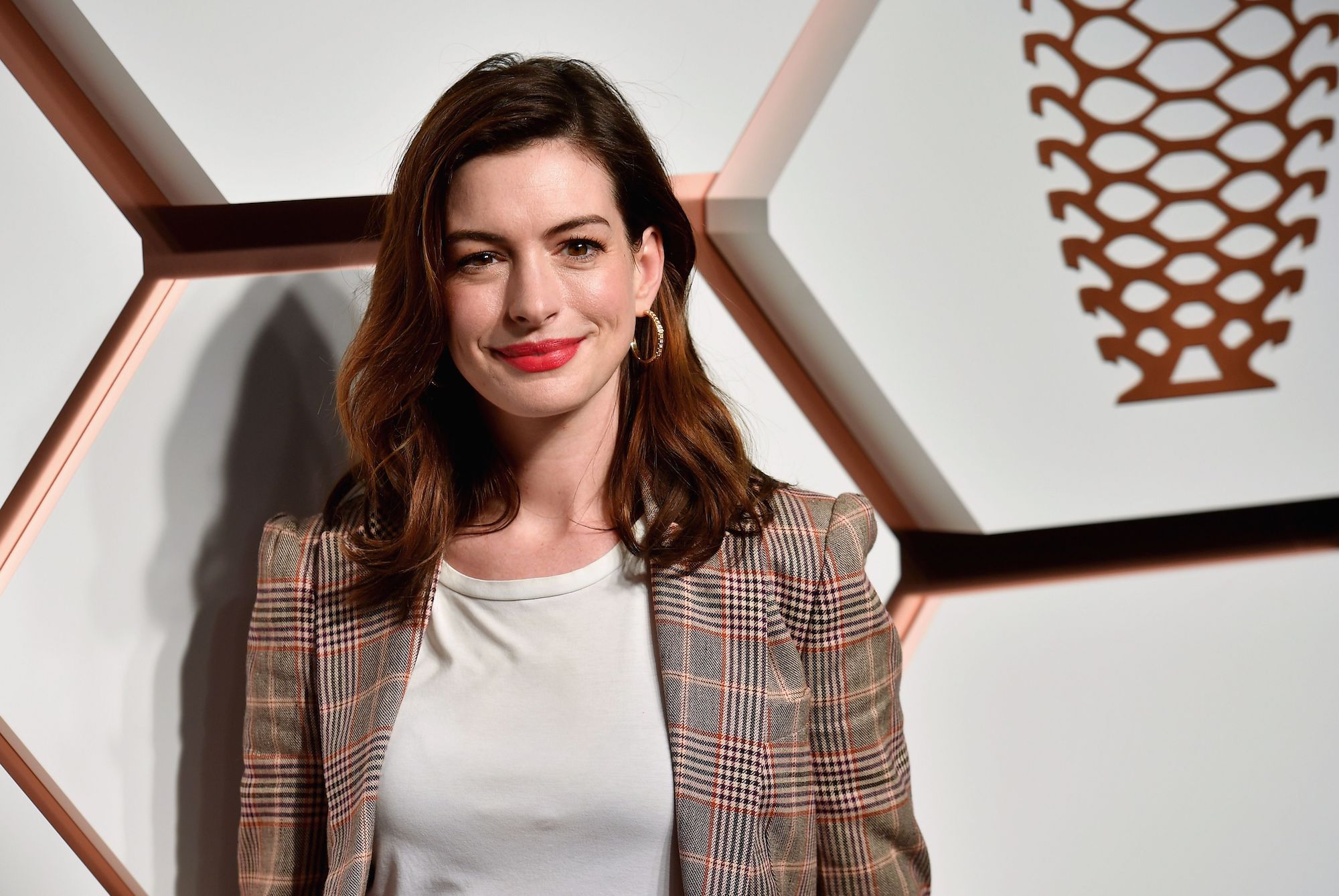 Anne Hathaway smiling in front of a geometric background
