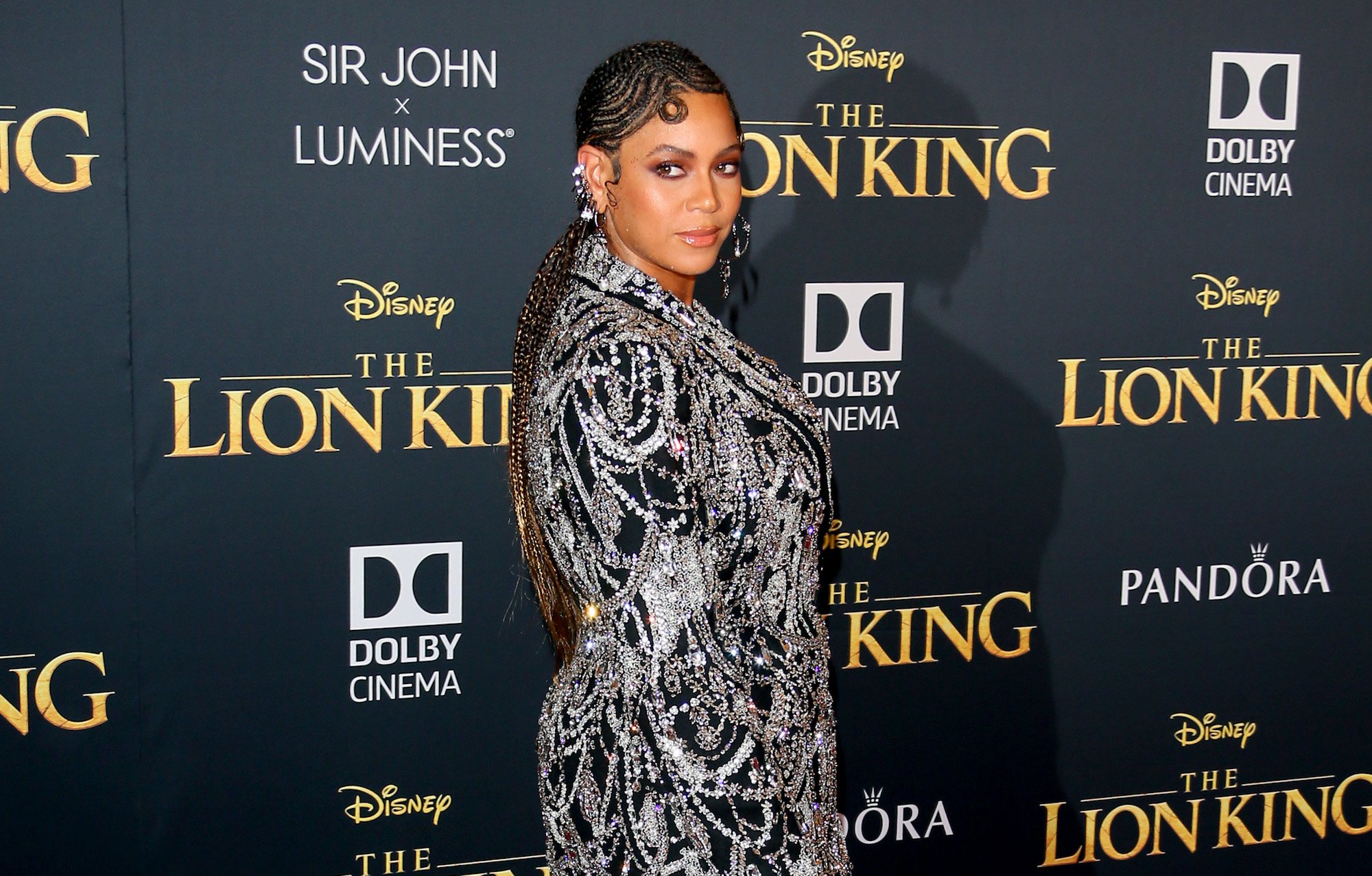 Beyoncé slightly smiling, looking back, in front of a black background with the 'Lion King' logo