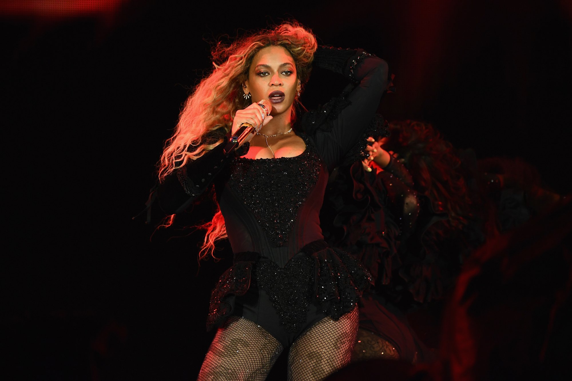 Beyoncé performing onstage, holding a microphone in one hand and adjusting her hair with the other