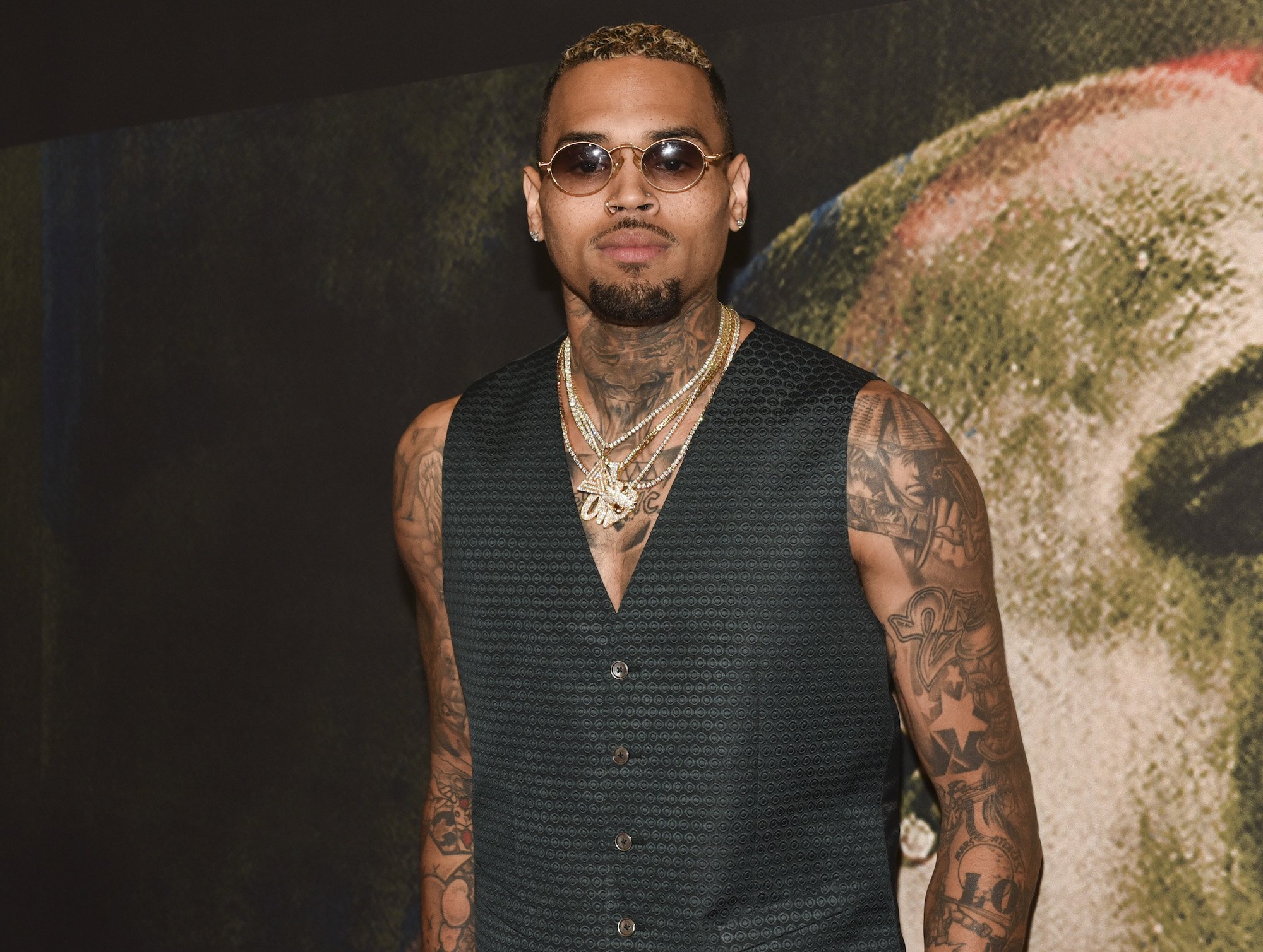 Chris Brown wearing sunglasses in front of a blurred background with an image