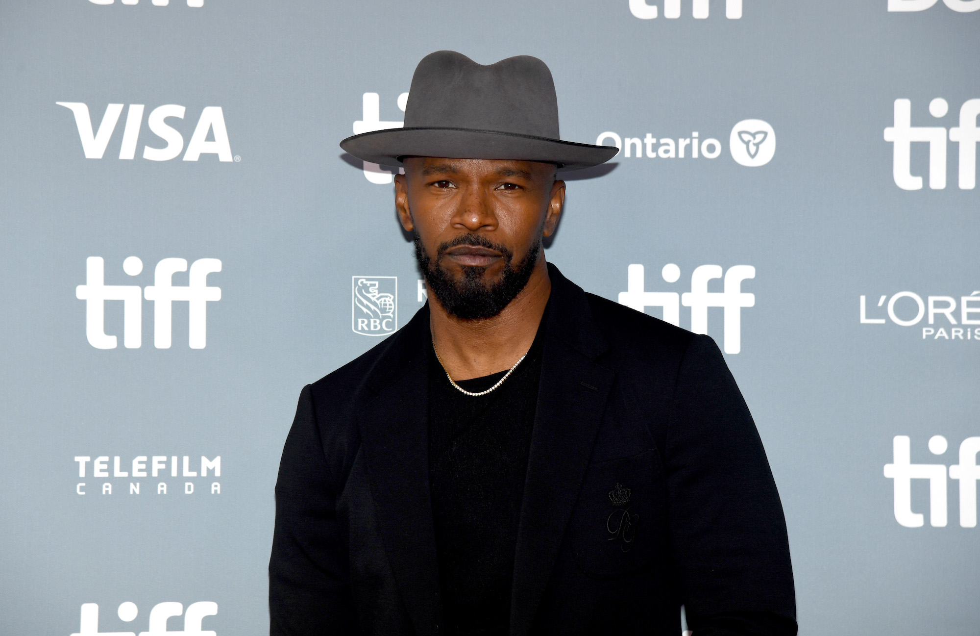 Jamie Foxx wearing a gray hat in front of a blue background with white lettering