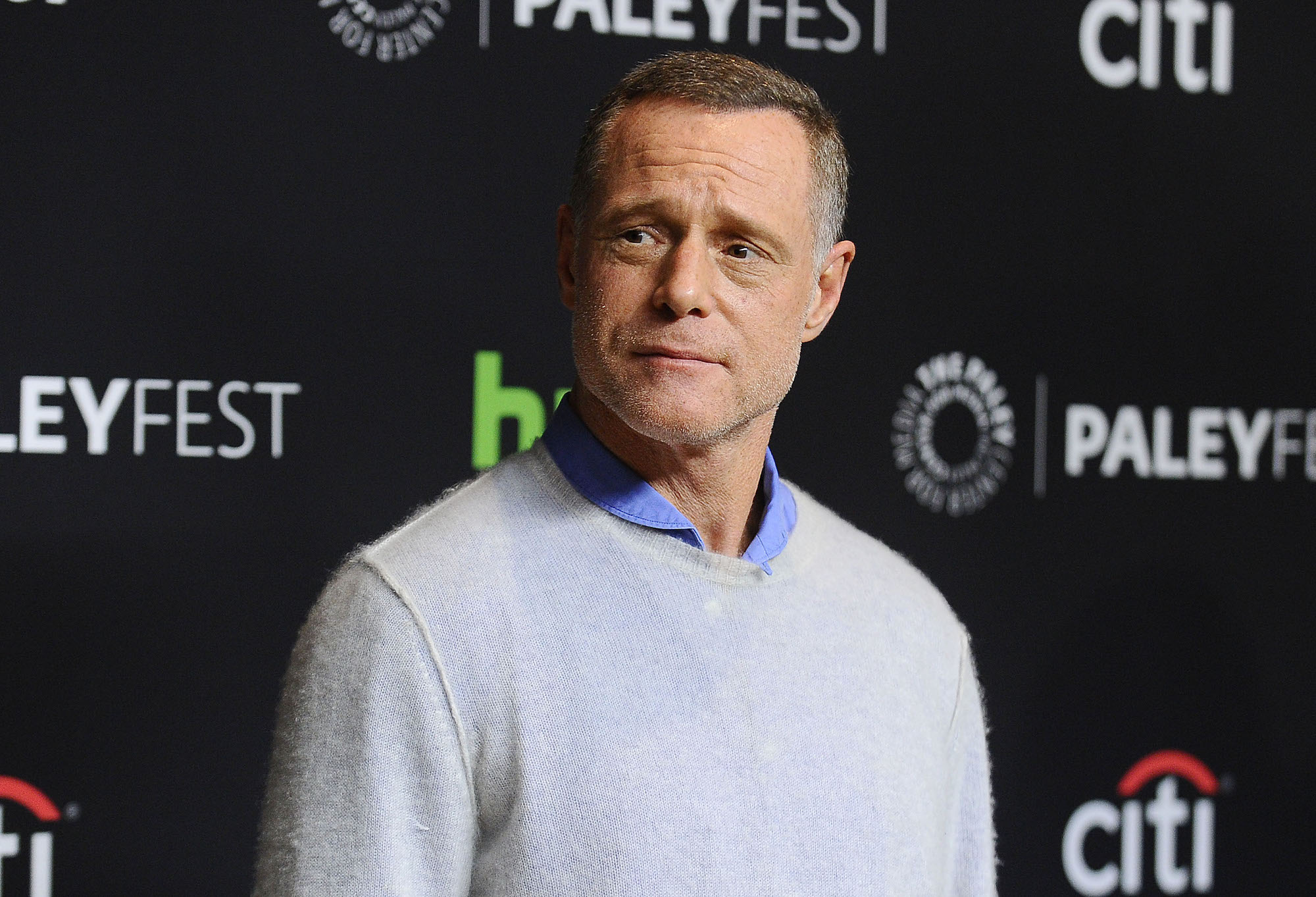 Jason Beghe slightly smiling, looking off to the side, in front of a black background
