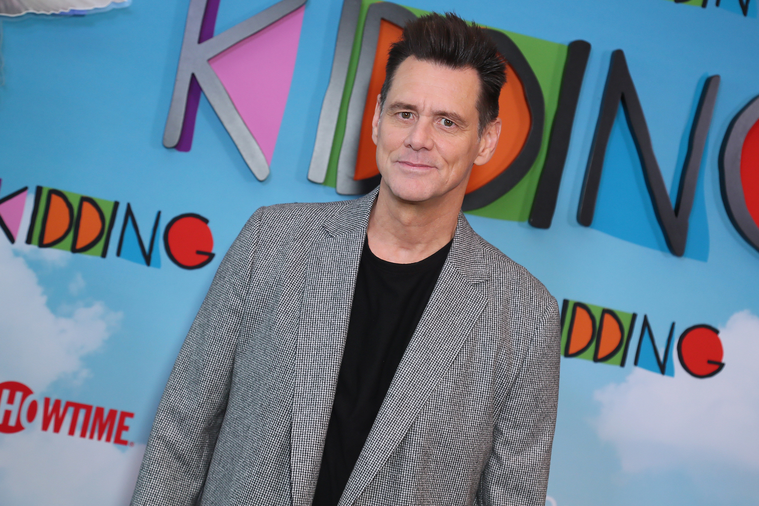 Jim Carrey smiling slightly in front of a multicolored background