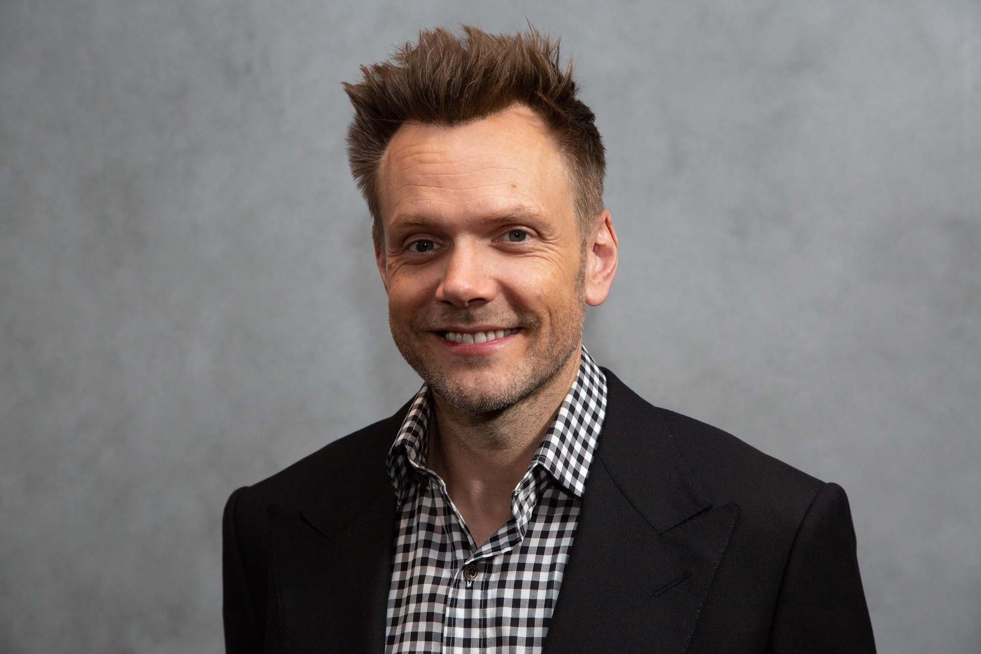 Joel McHale smiling in front of a gray background
