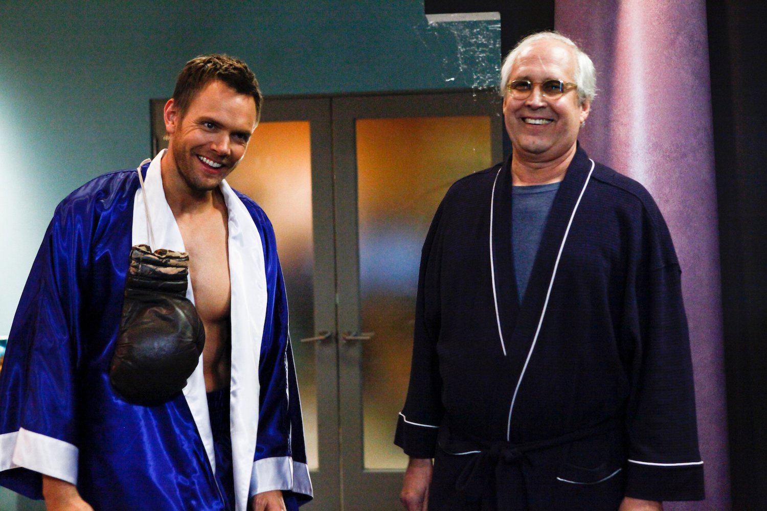 (L-R) Joel McHale and Chevy Chase laughing, wearing boxing robes