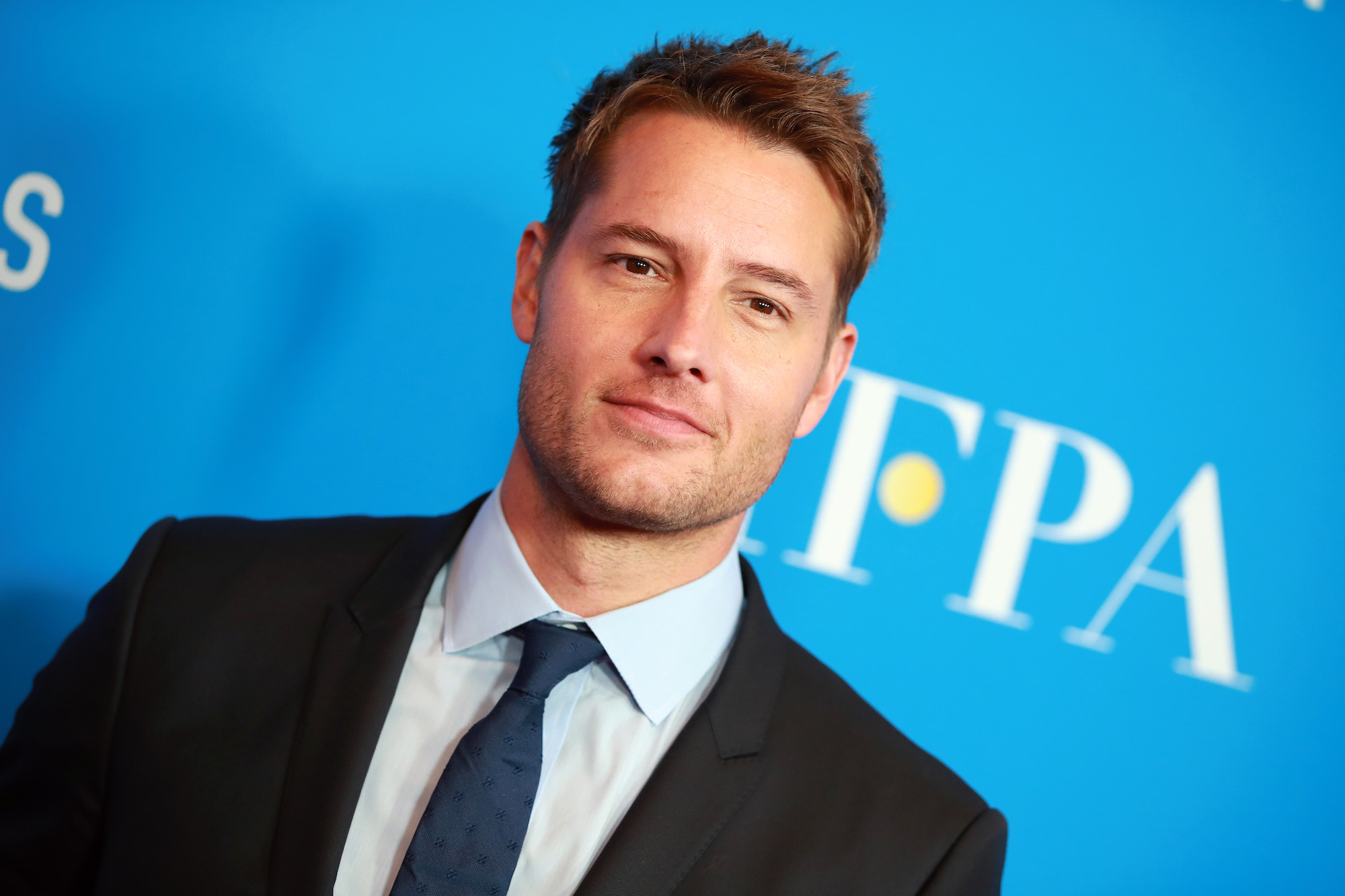Justin Hartley smiling in front of a blue background