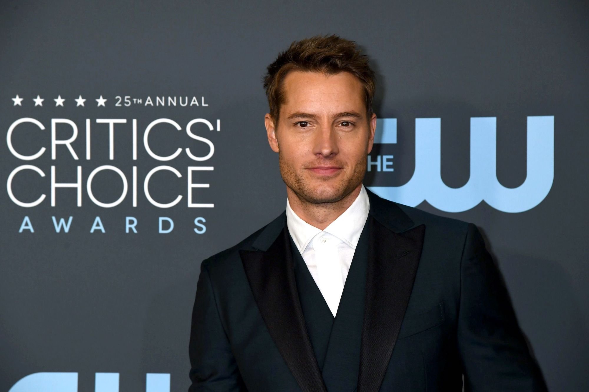Justin Hartley smiling in front of a gray background