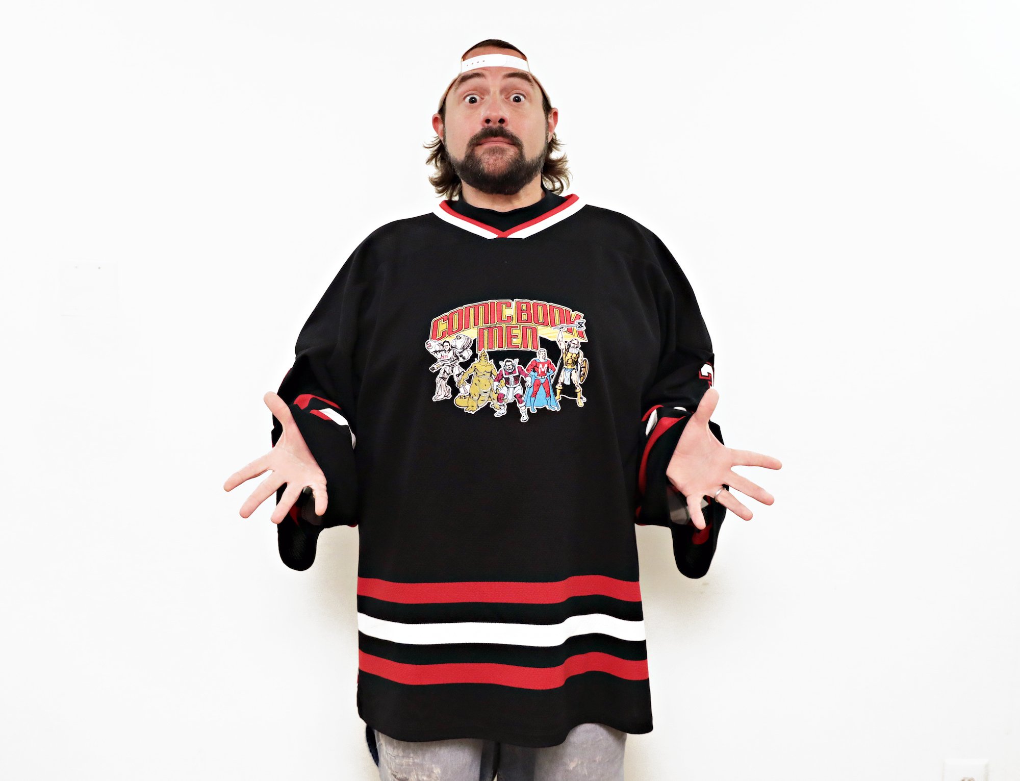 Kevin Smith shrugging, wide eyed and looking surprised, in front of a white background