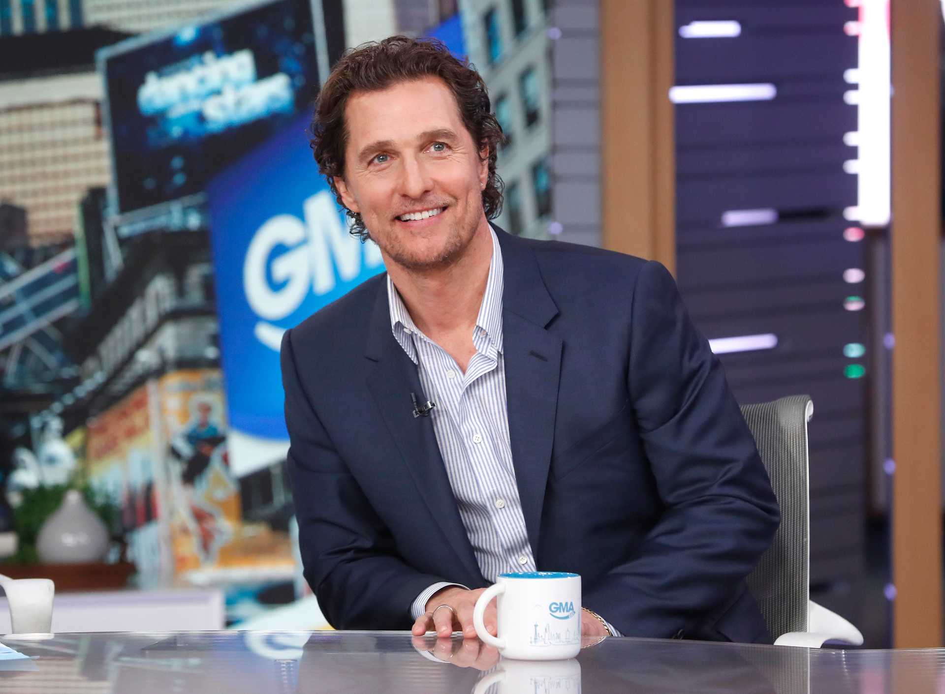 Matthew McConaughey in a dark blazer at a table with a cup