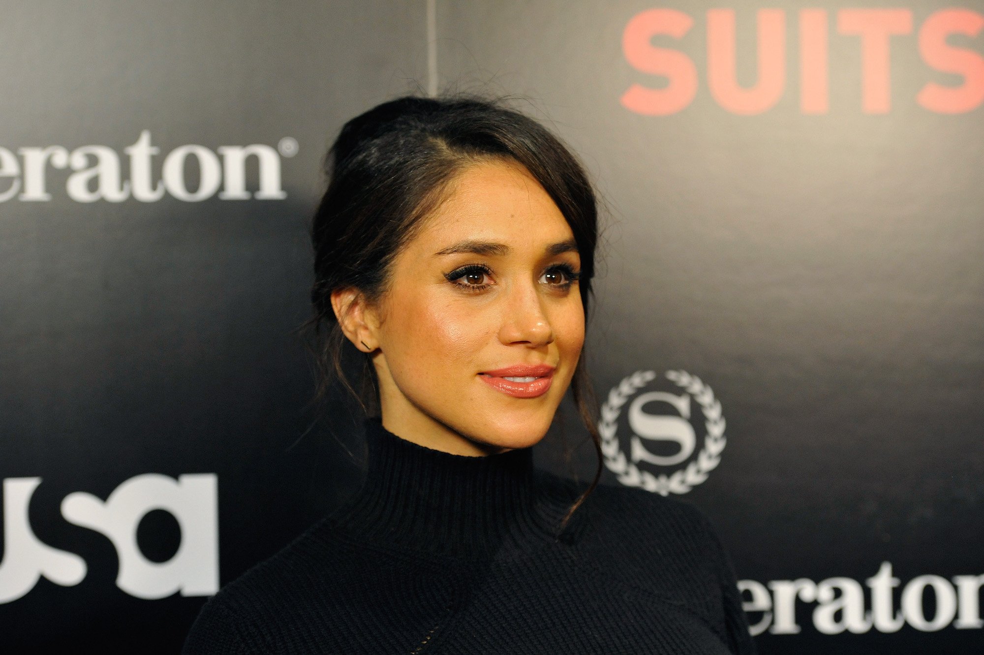 Meghan Markle smiling slightly in front of a black background