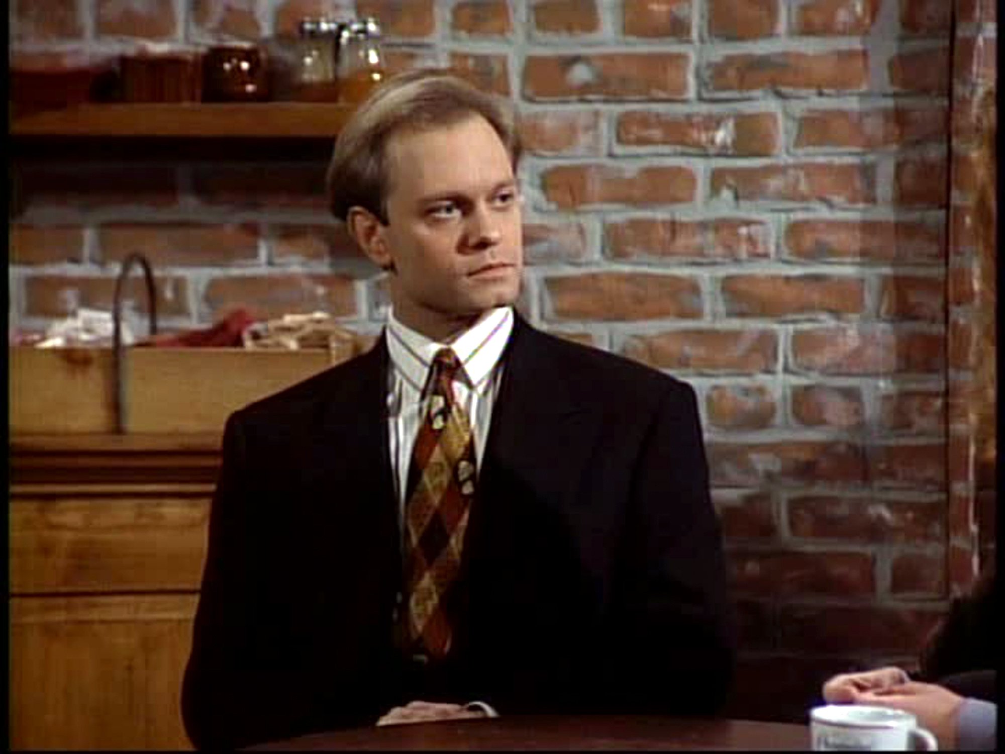 David Hyde Pierce as Dr. Niles Crane sits at a table in Cafe Nervosa