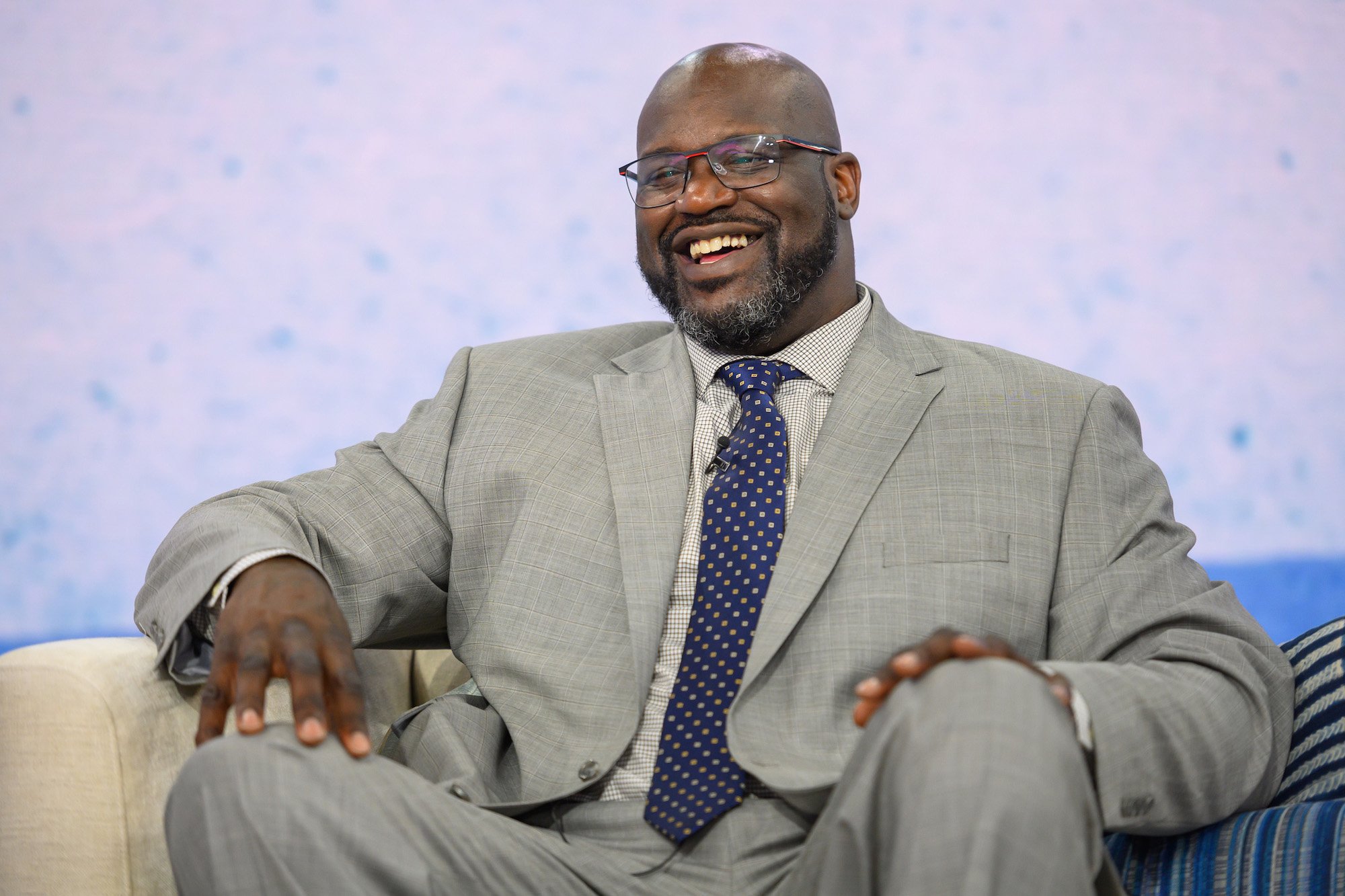 Shaquille O'Neal smiling, sitting down, in front of a white background