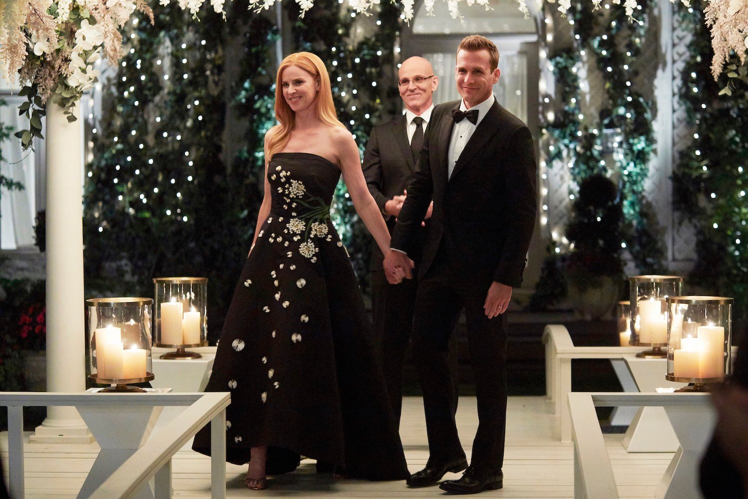 (L-R) Sarah Rafferty as Donna Paulsen, Ray Proscia as Dr. Stan Lipschitz, Gabriel Macht as Harvey Specter smiling around an altar